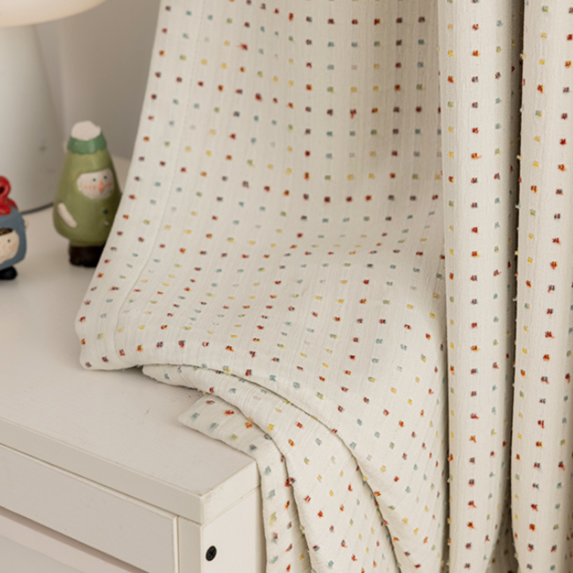 Colorful dotted room darkening kids curtains over a surface with decorative items in the background