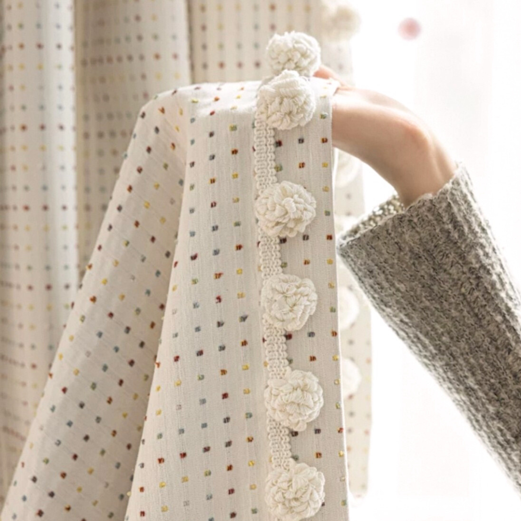 Beige curtains with dotted woven patterns and pompom side trim.