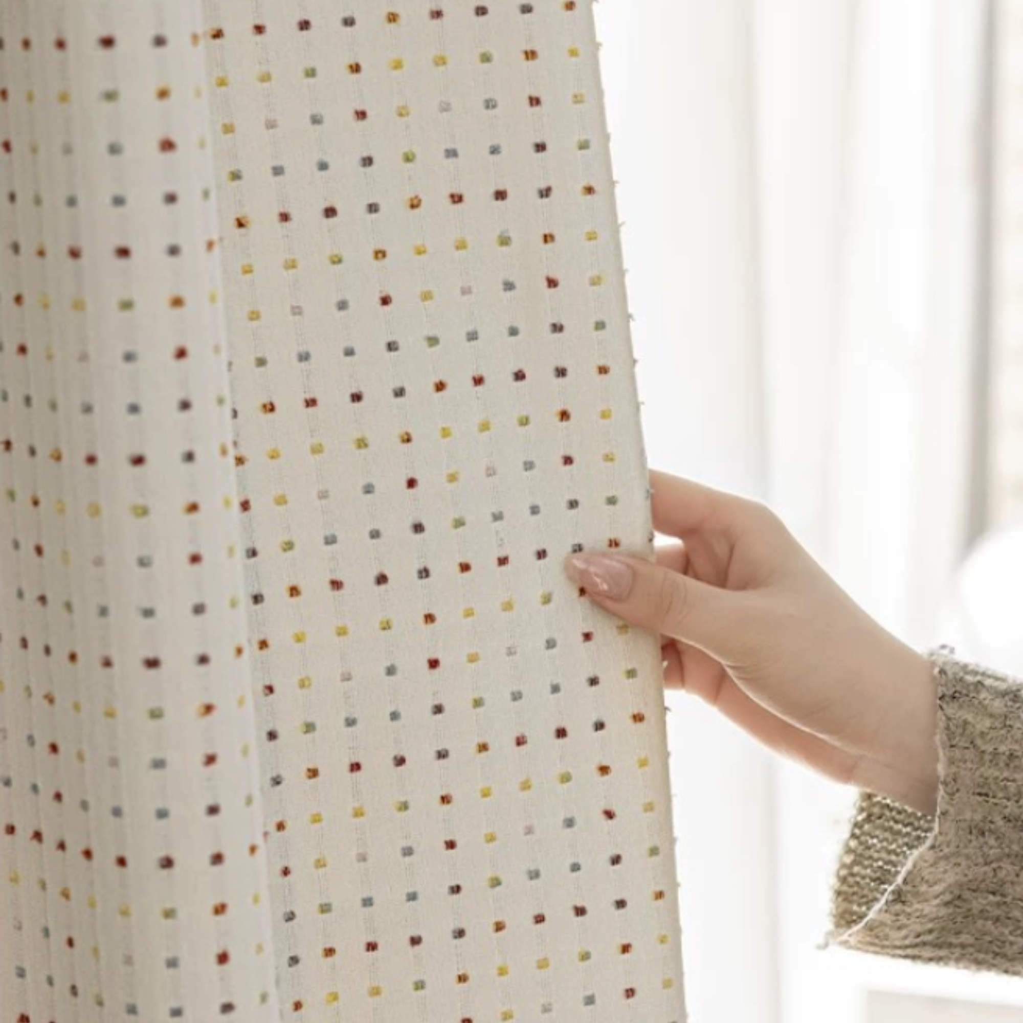 Hand touching room darkening kids curtains with textured fabric and a subtle colorful patterned, blurred background