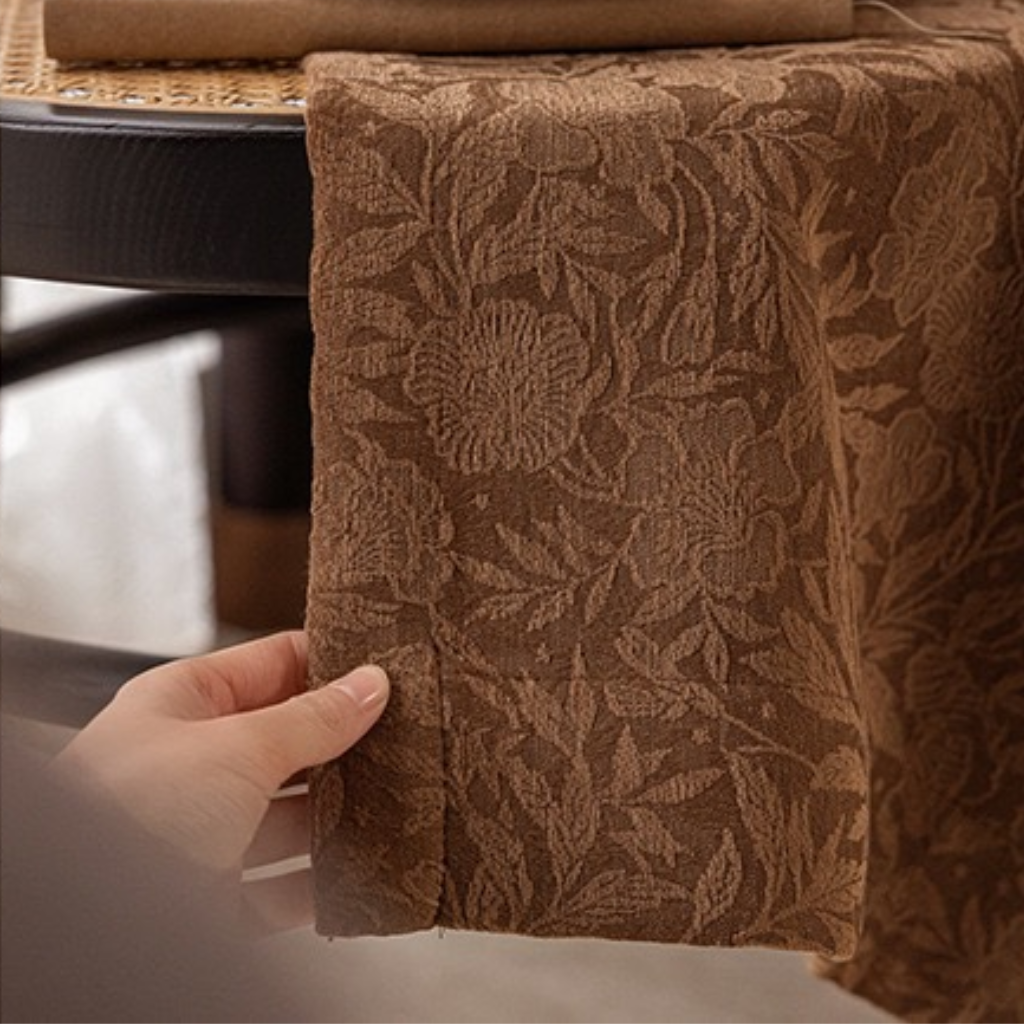 Brown textured fabric with floral pattern held by a hand, on a blurred background