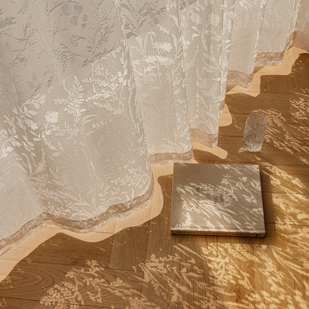 Sheer white lace curtain with casting floral patterned shadow on a wooden floor