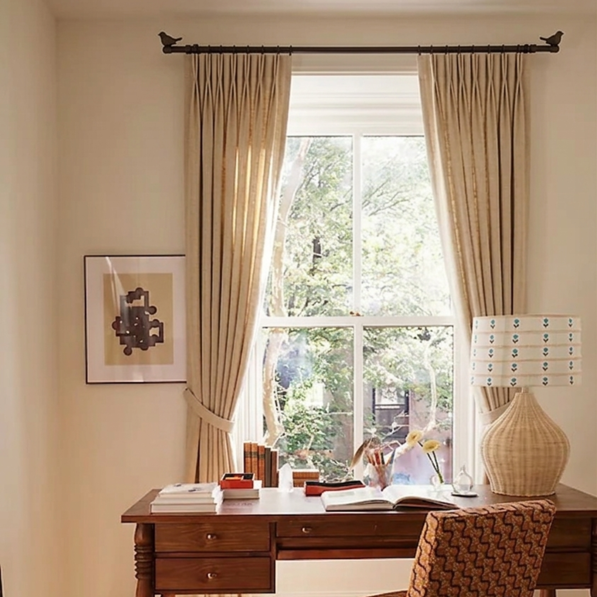 Home office with a wooden desk, chair, and large window with curtains on a bird detailed curtain rod.