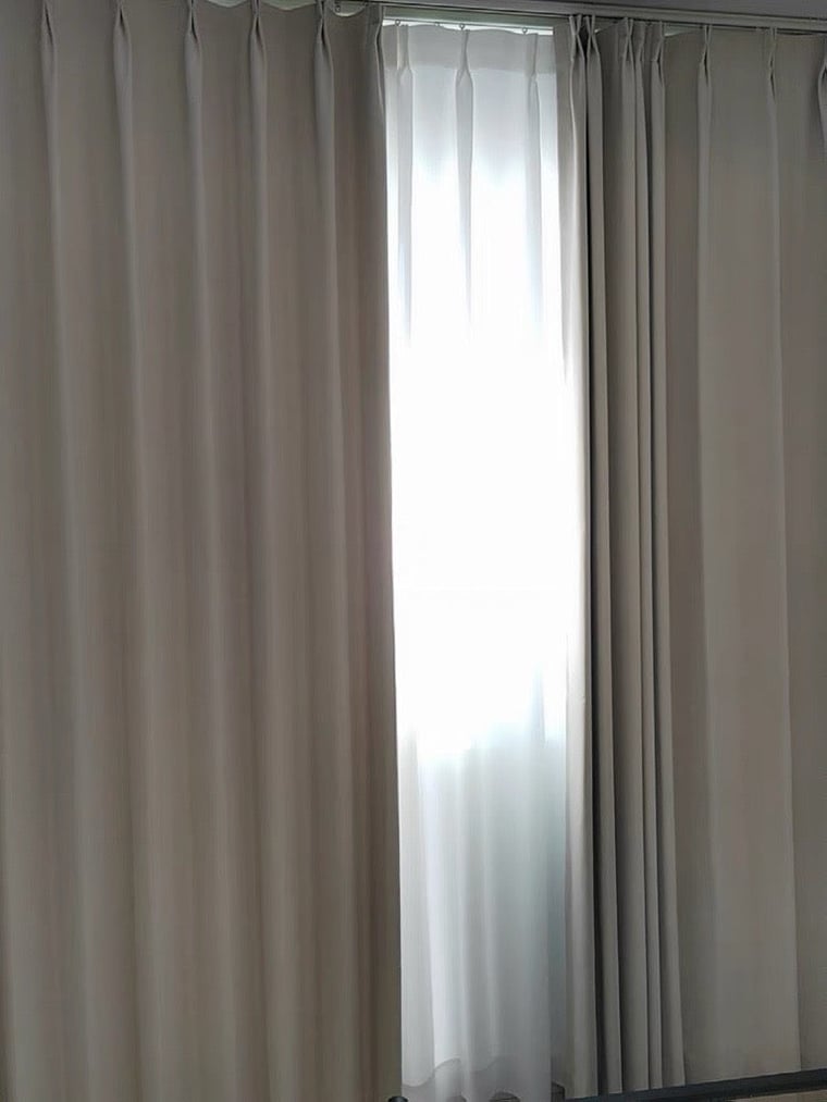 Beige blackout curtains with a blurred window in the background