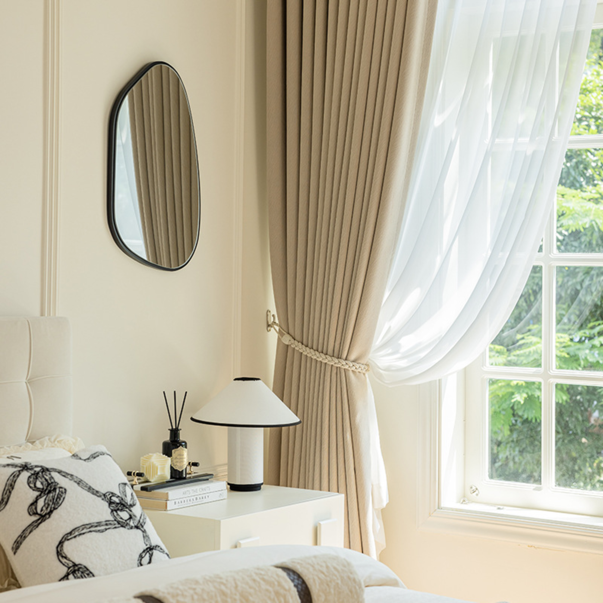 Neatly arranged bedroom with beige herringbone curtains, a lamp, and decorative items.