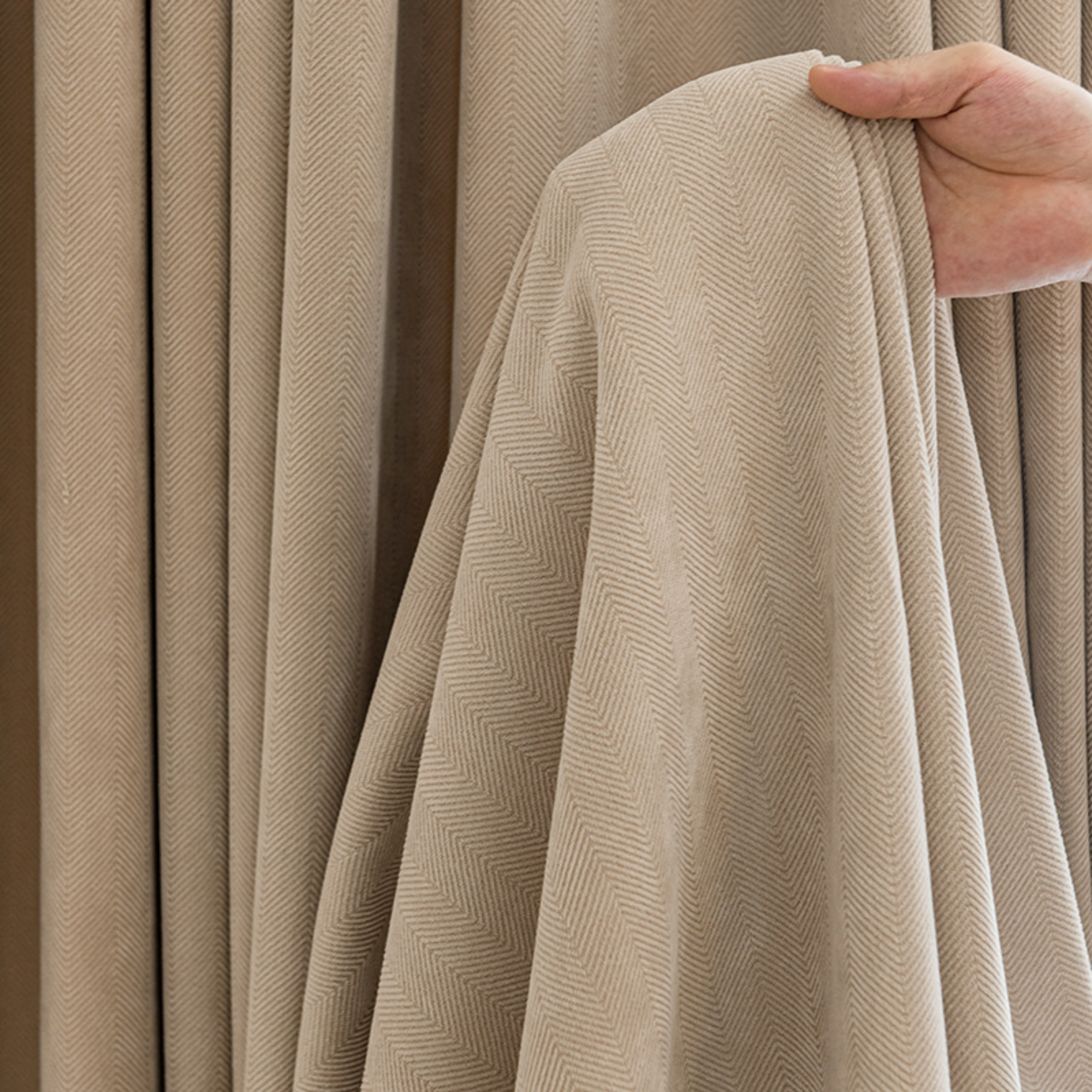 Beige herringbone curtain fabric held by a hand showing its texture.