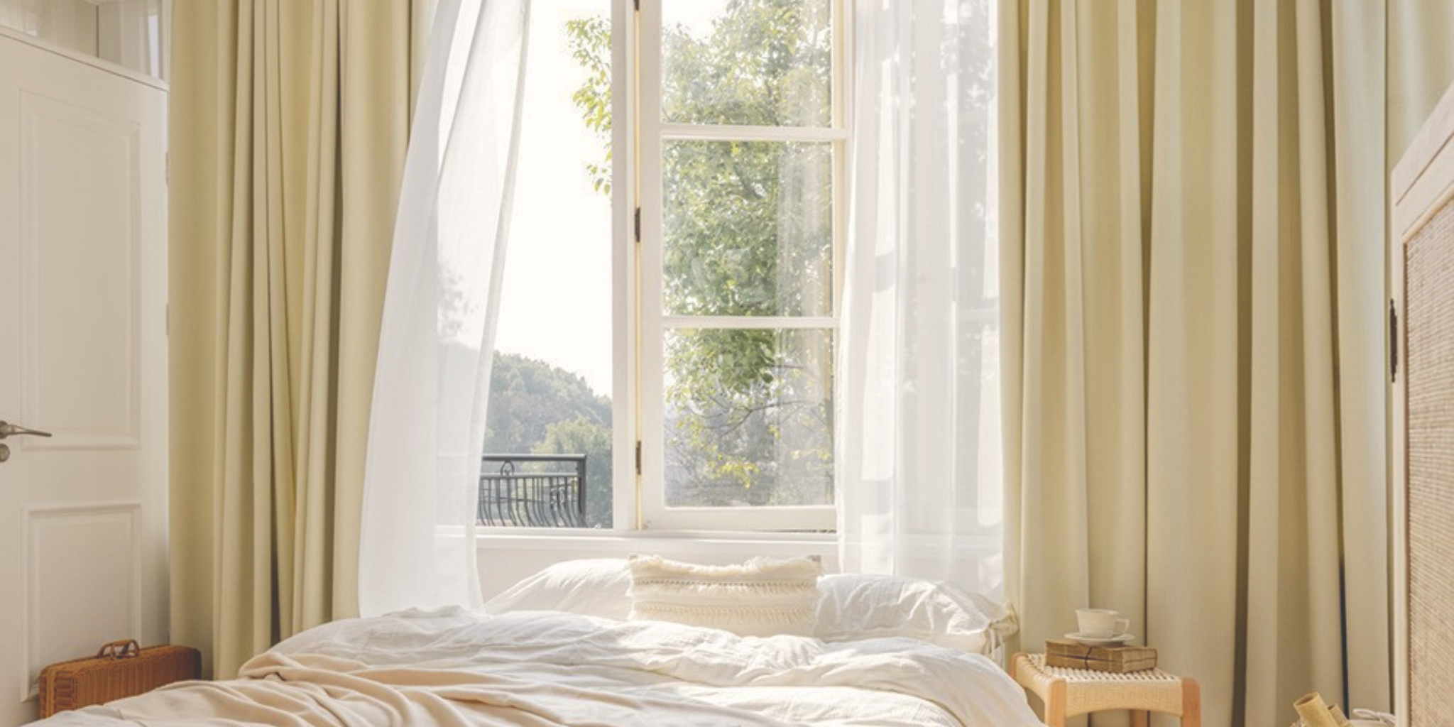 Bedroom with a large window draped with custom beige curtains and white sheers.