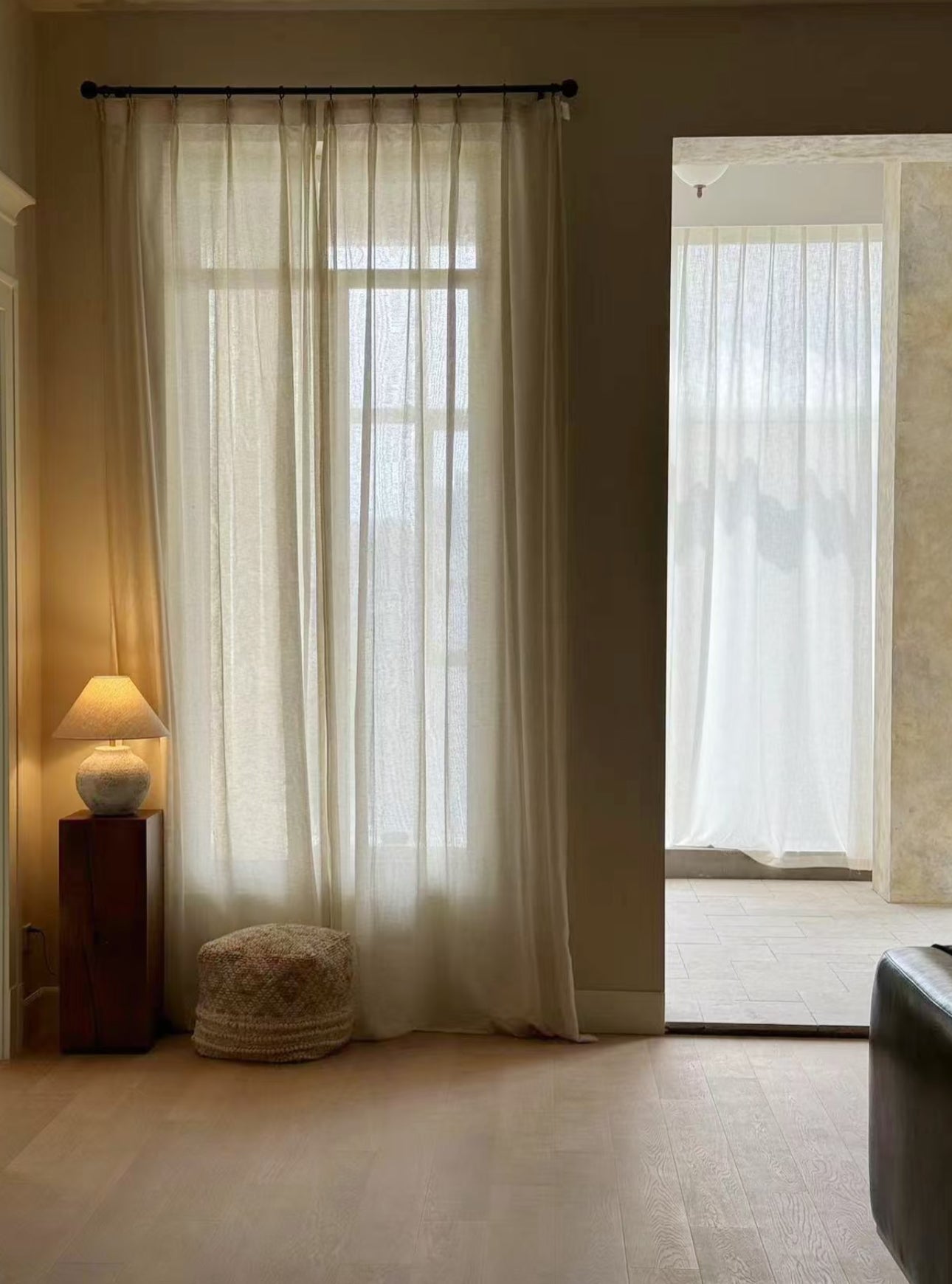 Linen sheer curtains in a room with a lamp and small table.