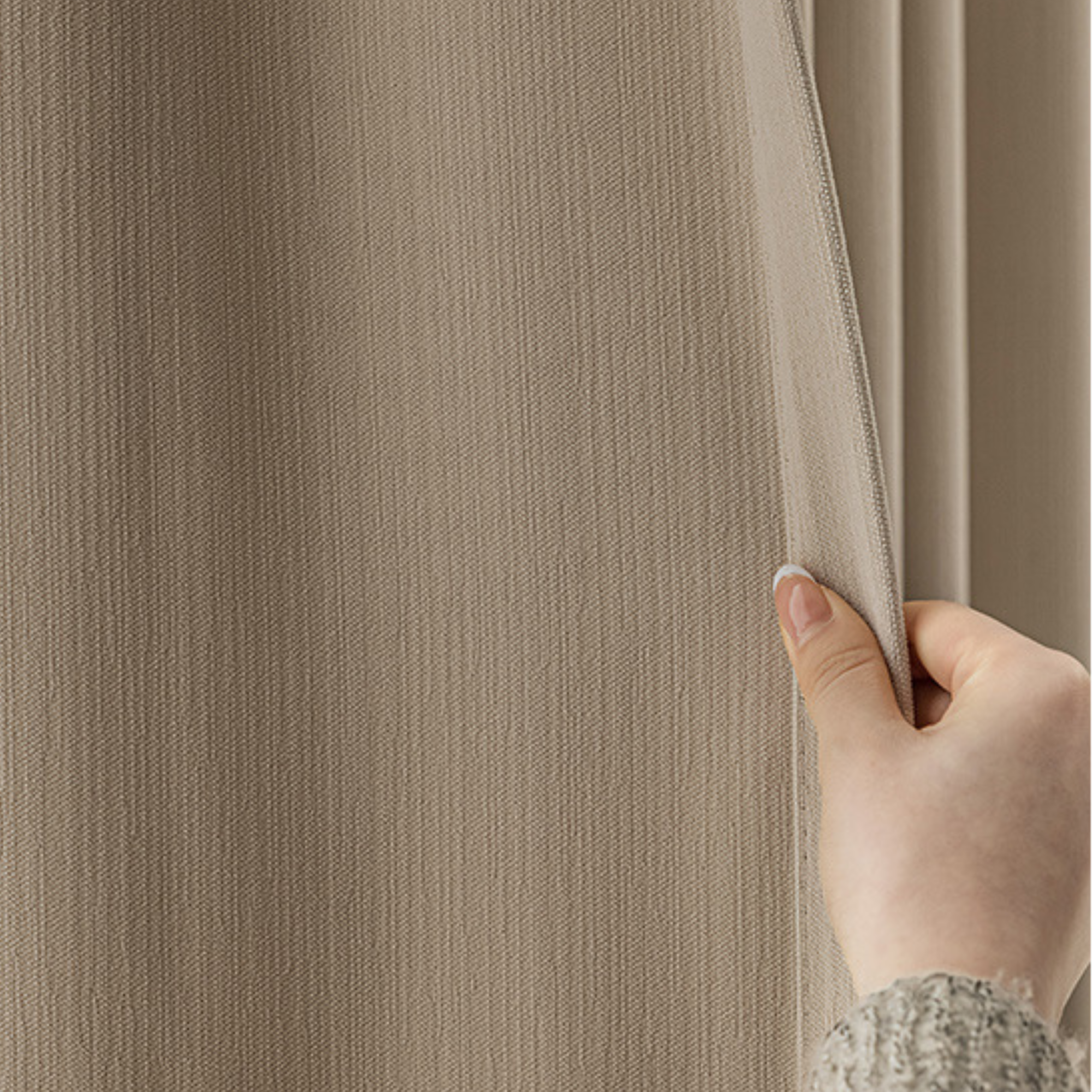 Hand pulling back a beige textured blackout curtain