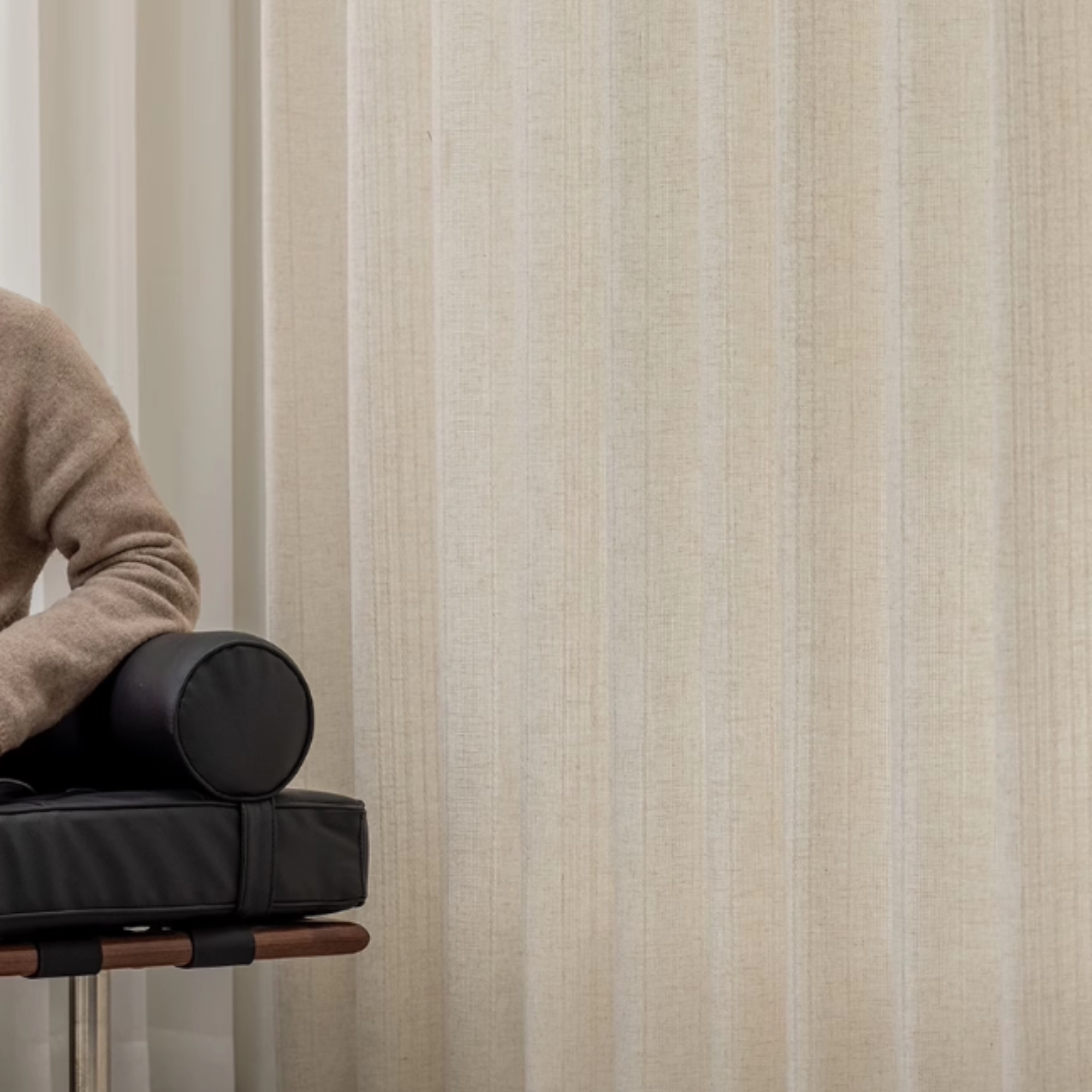 Person sitting on a chair with black cylindrical objects against a cream striped linen curtains.