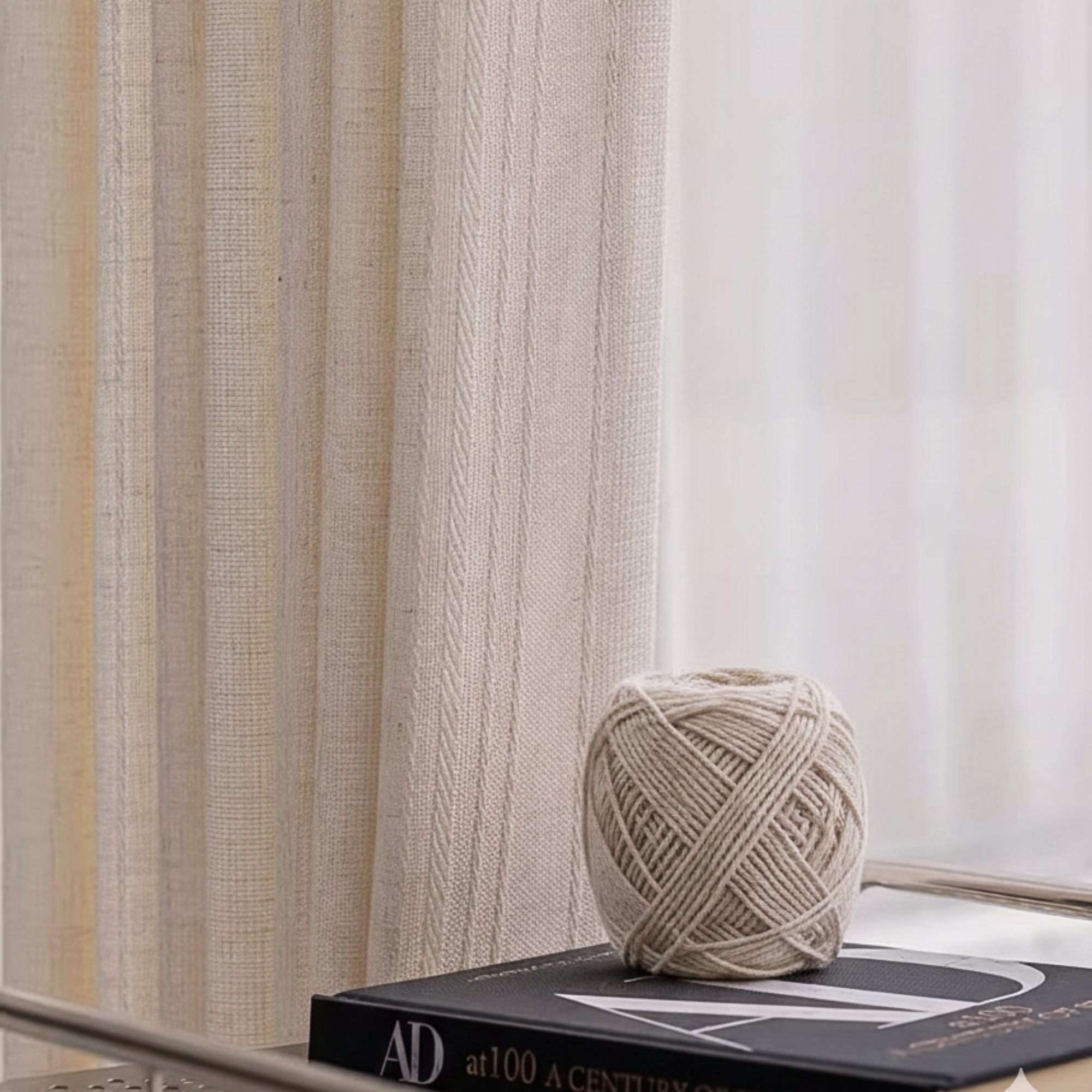 Ball of linen yarn on a book with beige linen curtains with weaving details in the background