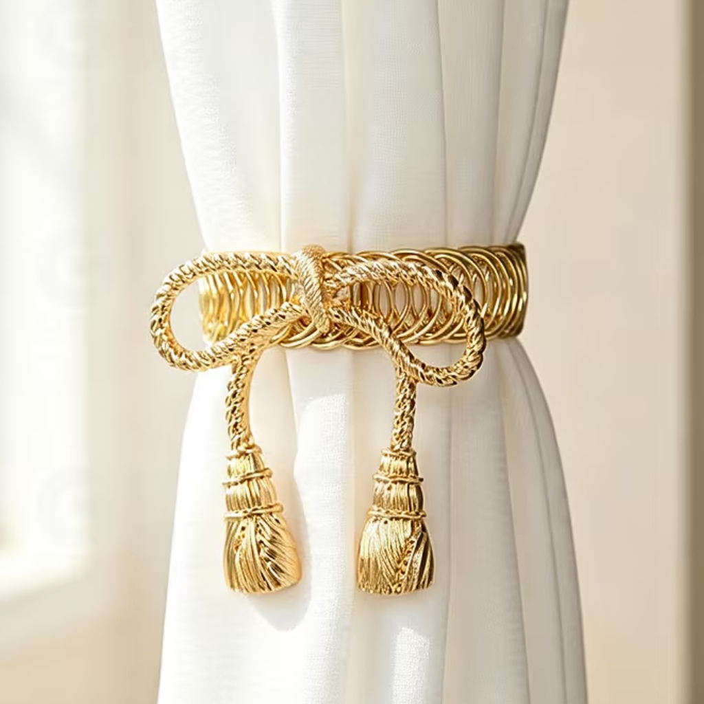 A gold curtain tieback with a braided rope design and tassels, tied around a white curtain panel.