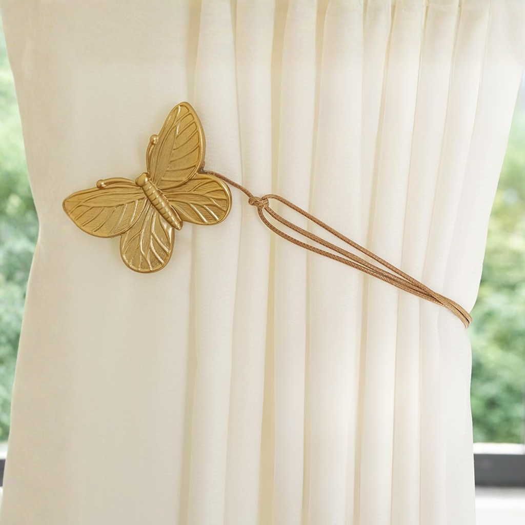 Gold butterfly-shaped curtain tieback on a white curtain with a blurred green outdoor background
