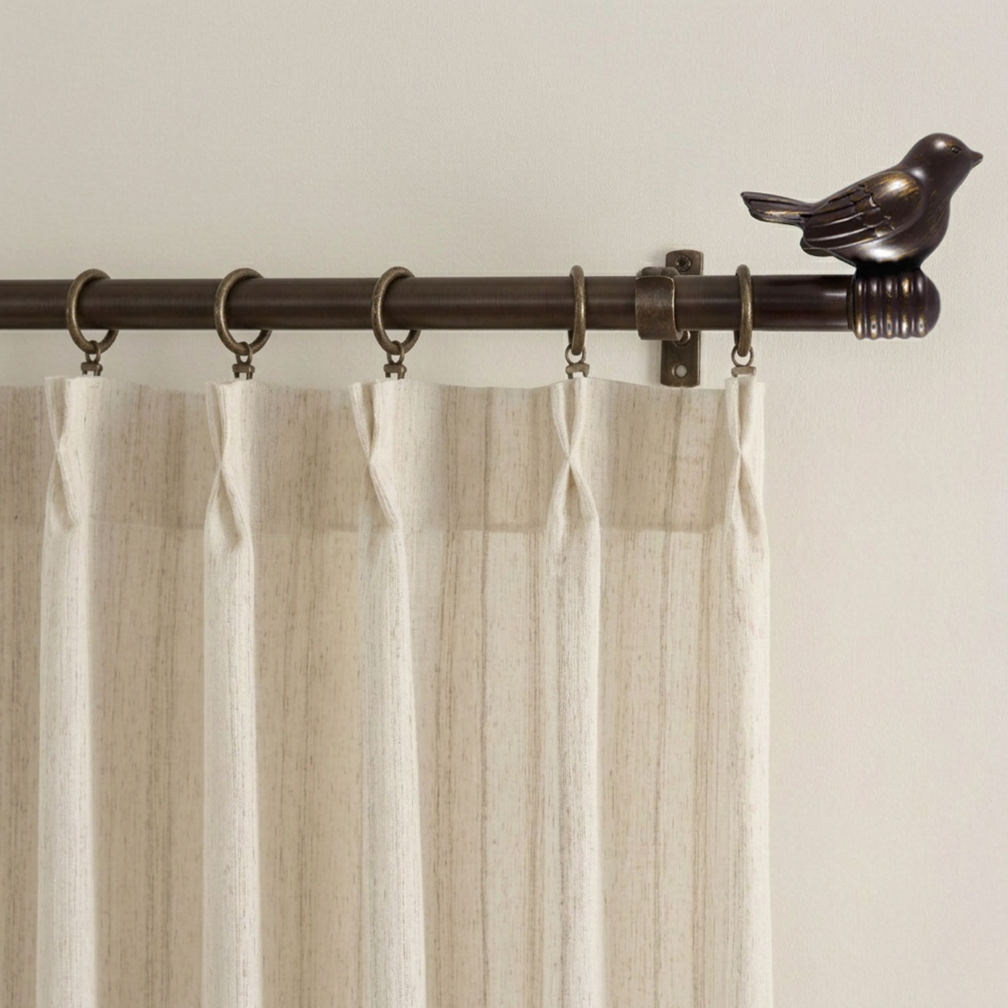 Curtain rod with decorative bird finial and rings holding a beige curtain against a neutral wall.