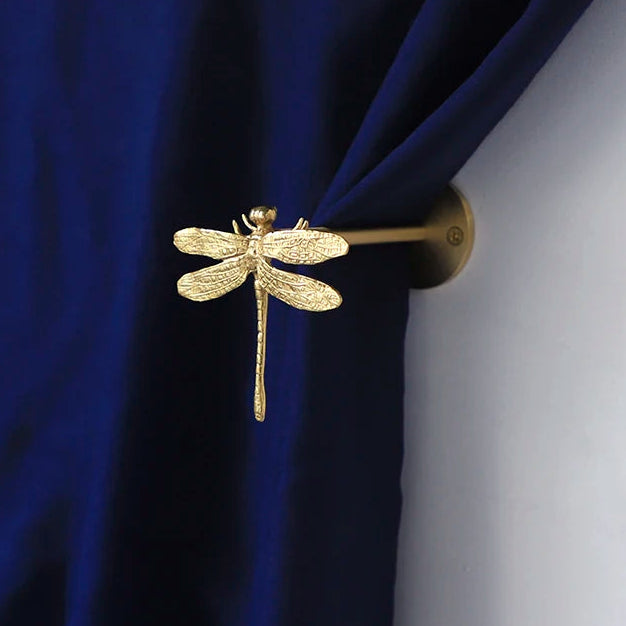 Gold dragonfly-shaped curtain hook on a blue curtain.