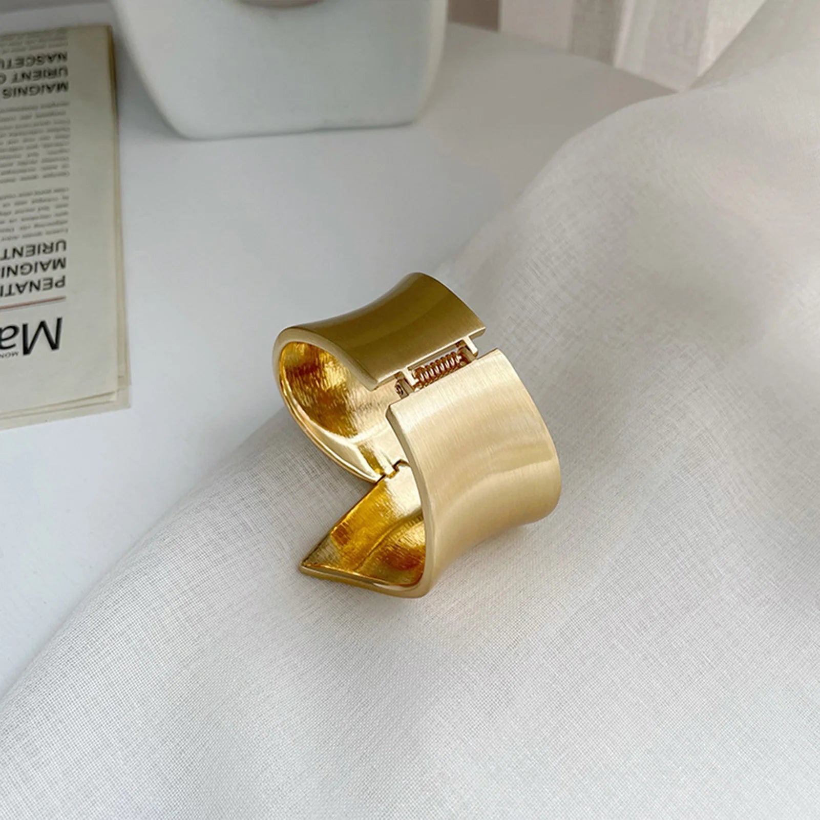 Gold cuff curtain tieback on a white fabric surface with a blurred background