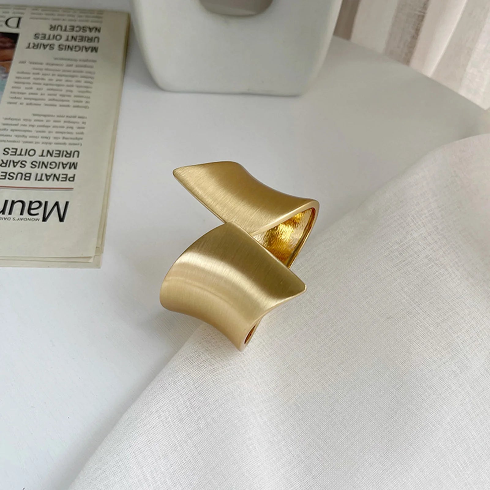 Brushed gold cuff curtain tieback on a white surface with a blurred newspaper in the background