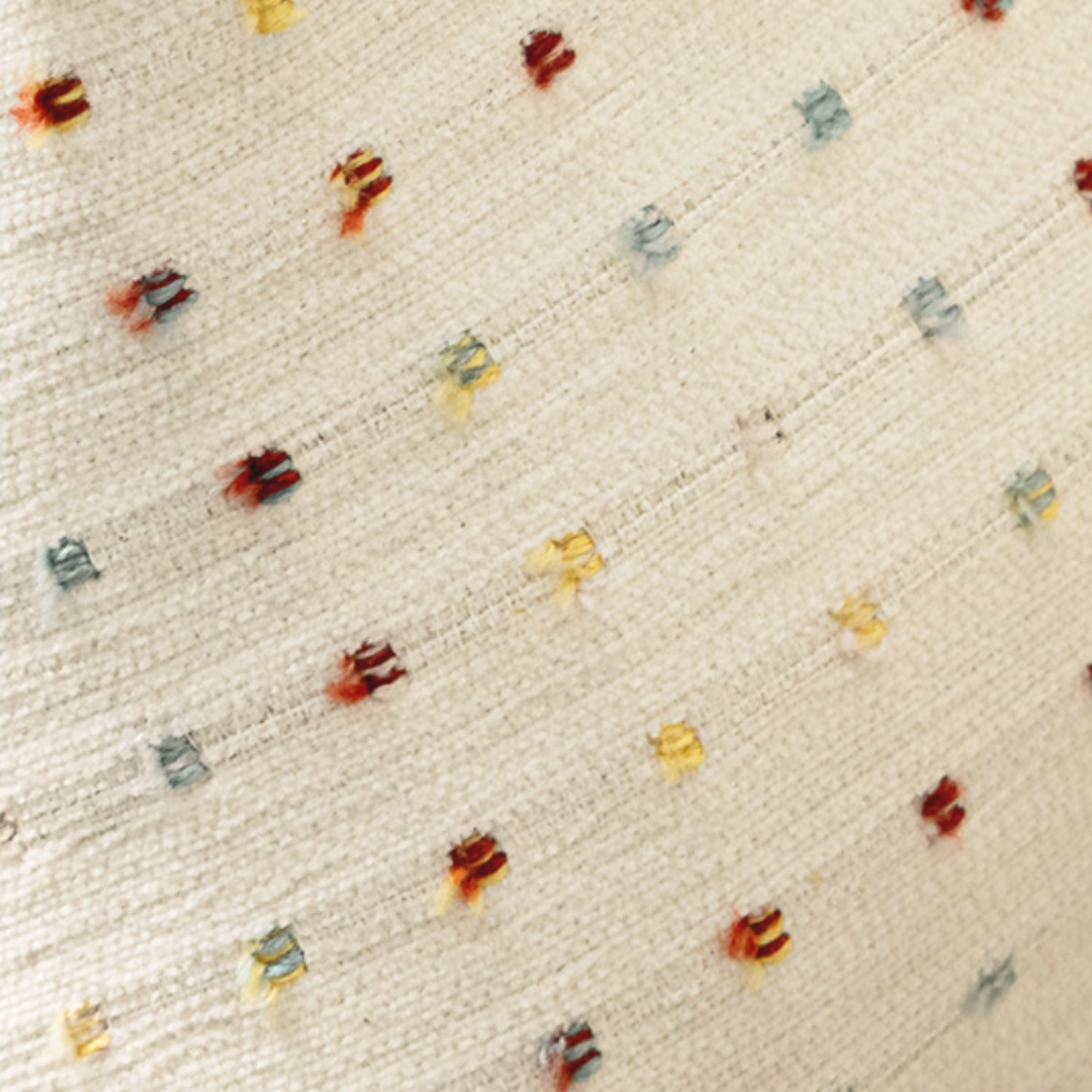 Close-up of a textured fabric with small colorful patterns on a beige curtain