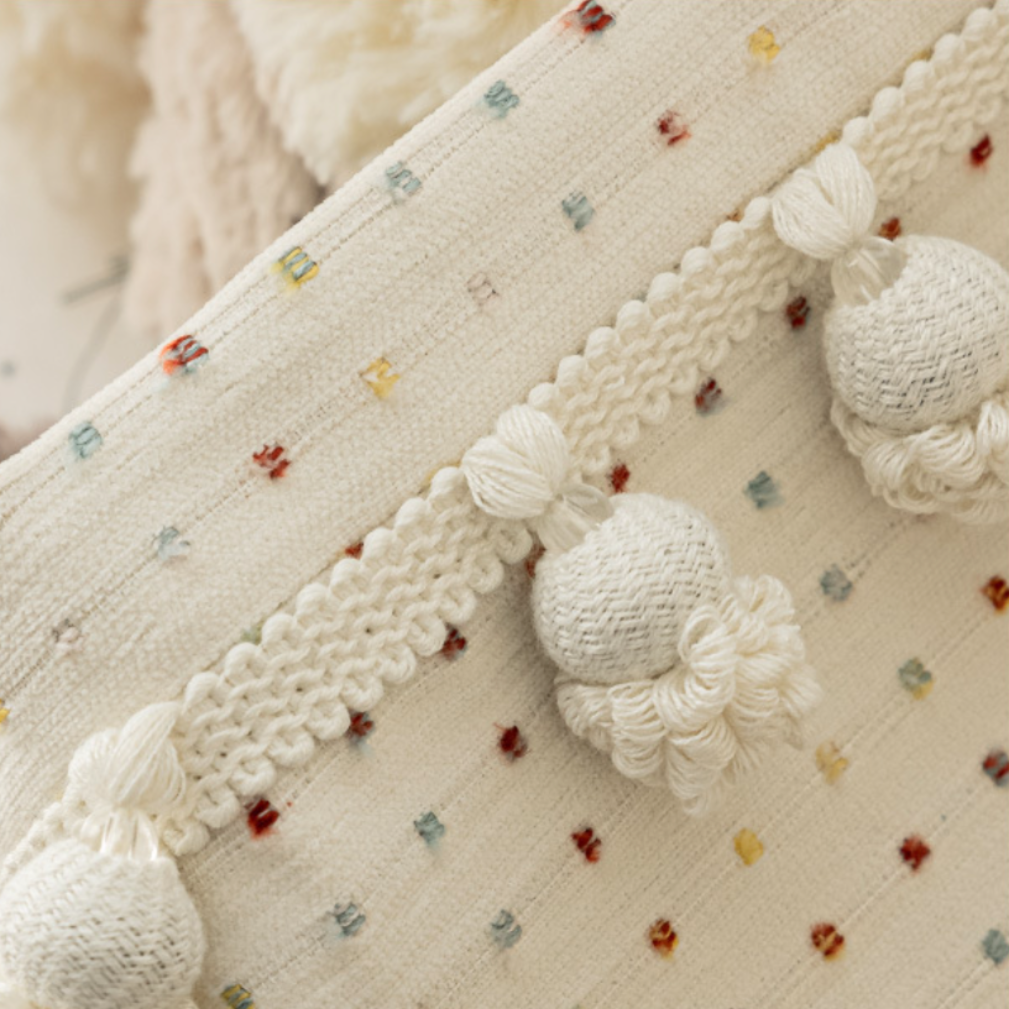 Close-up of a textured fabric with white knitted balls and colorful polka dot pattern