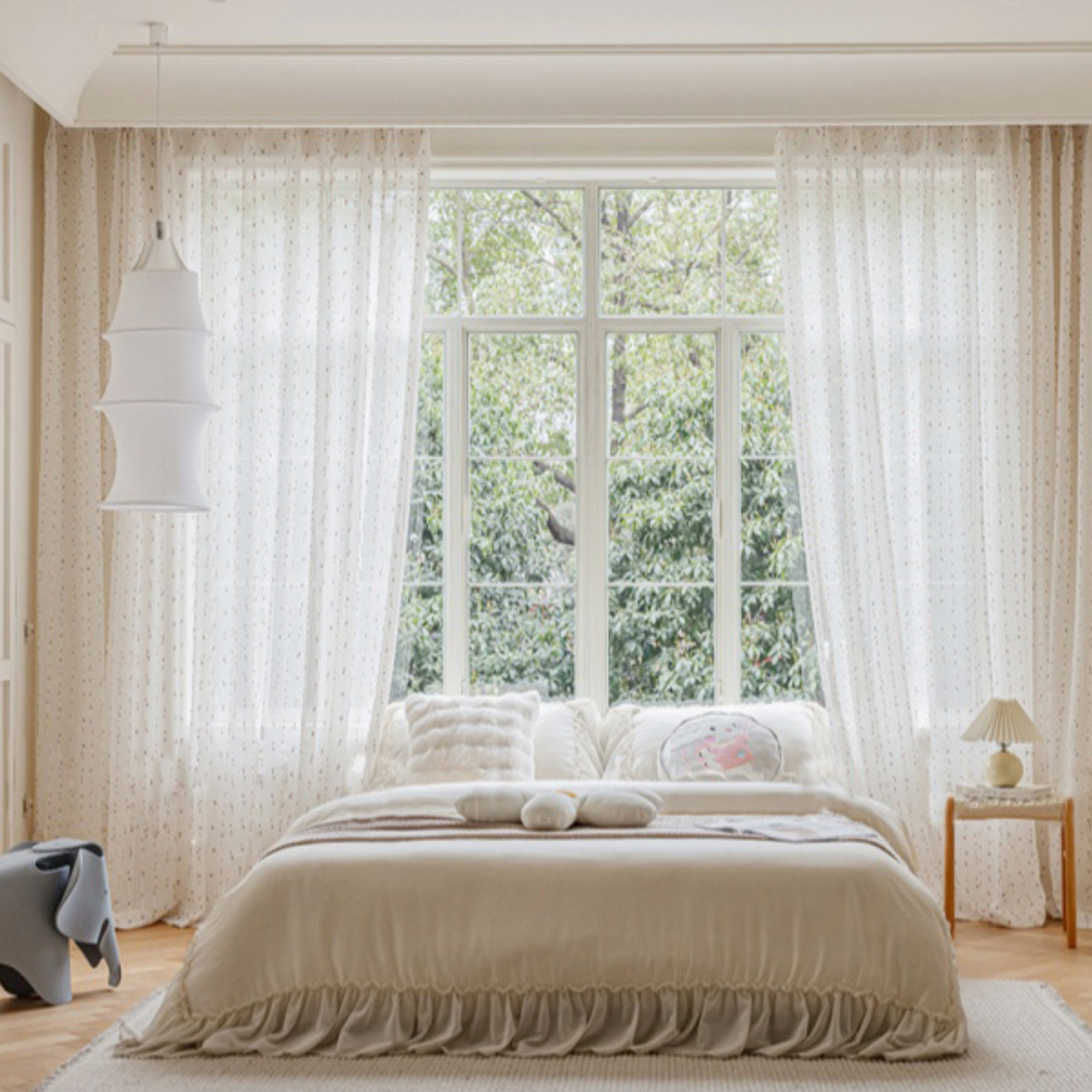 Neatly made bed in a bright kid's bedroom with large windows and beige curtains.