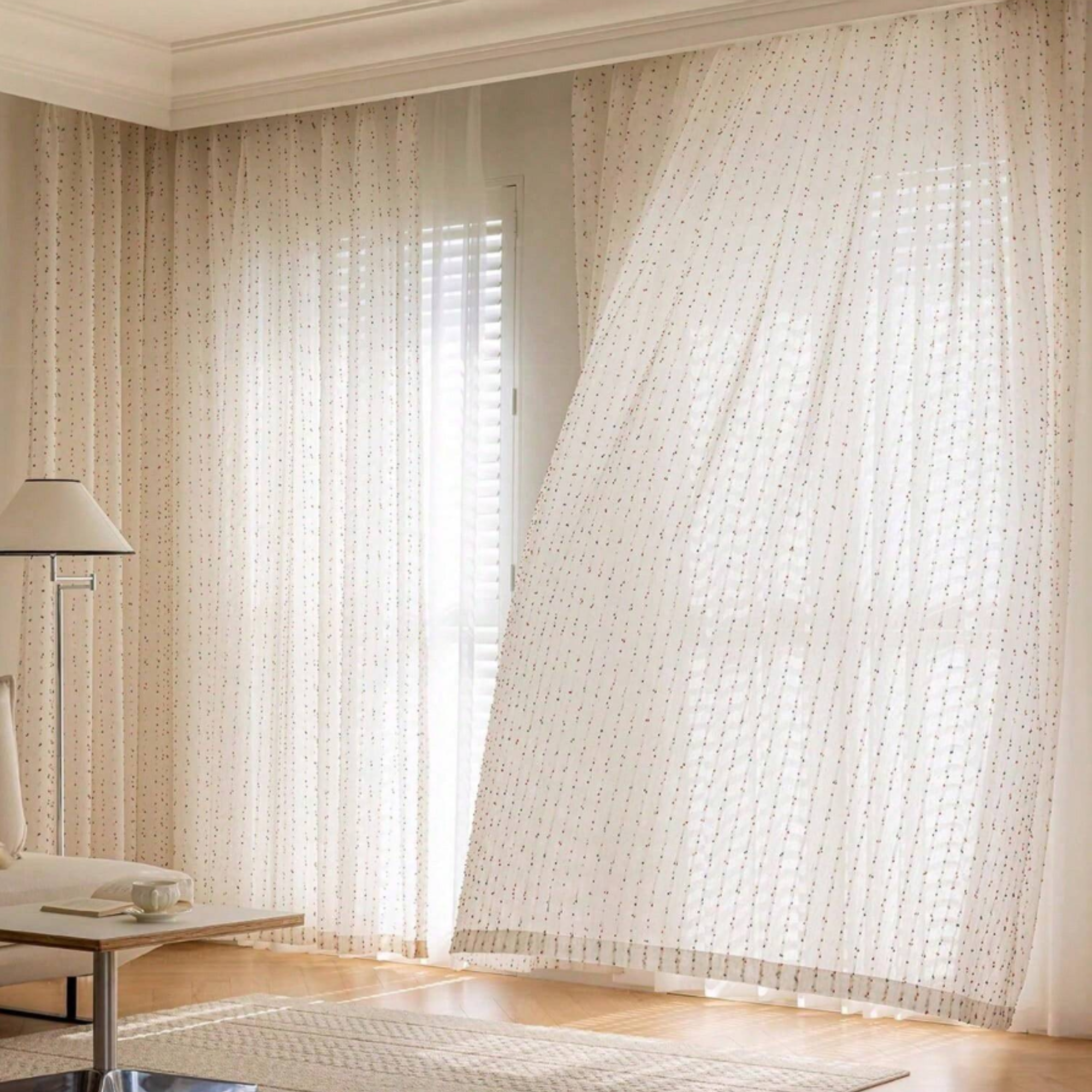 Sheer curtains with a subtle pattern gently filter light through in a room with a lamp and table.