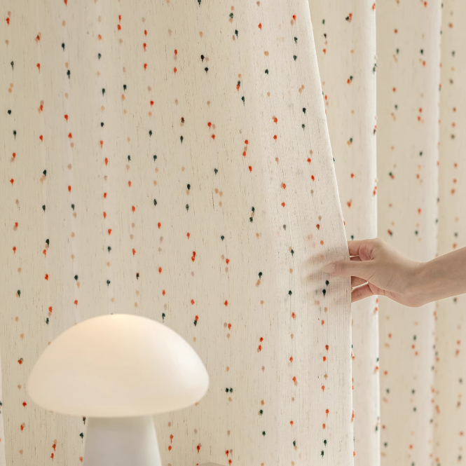 Hand touching a polka dot curtain with a white lamp in the foreground