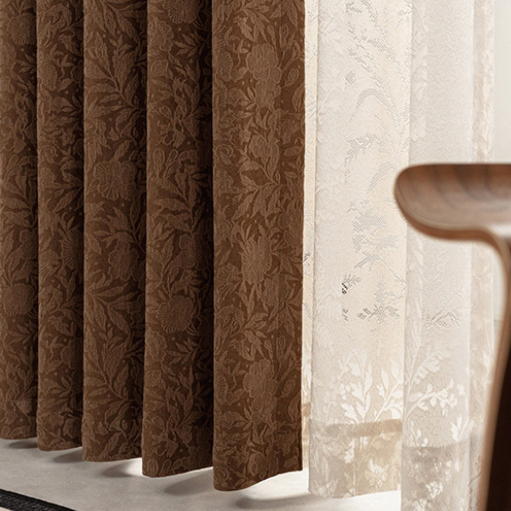 Brown patterned blackout curtain next to a sheer white curtain with a wooden chair.