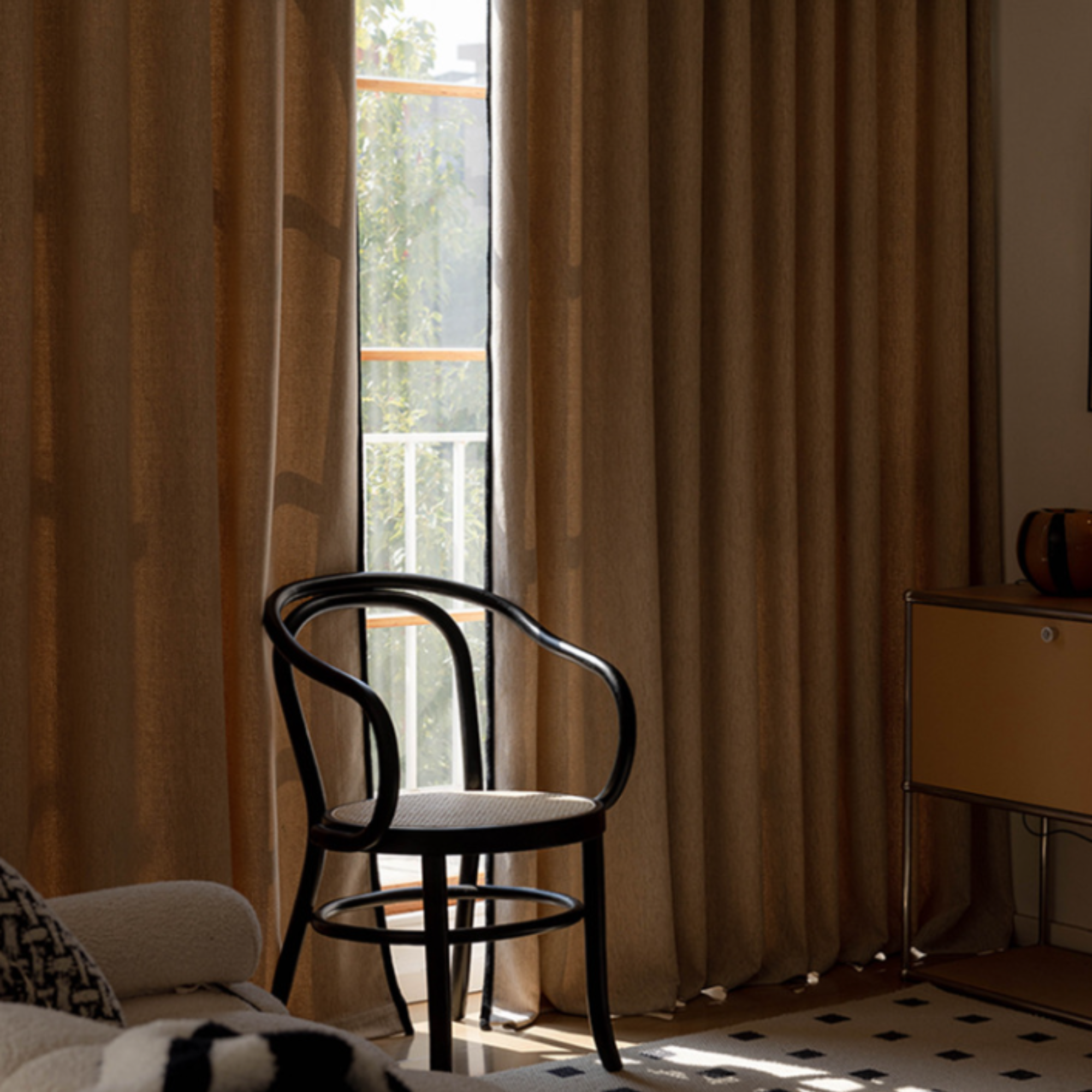Room interior with a black chair, beige curtains with black trim, and a side table.