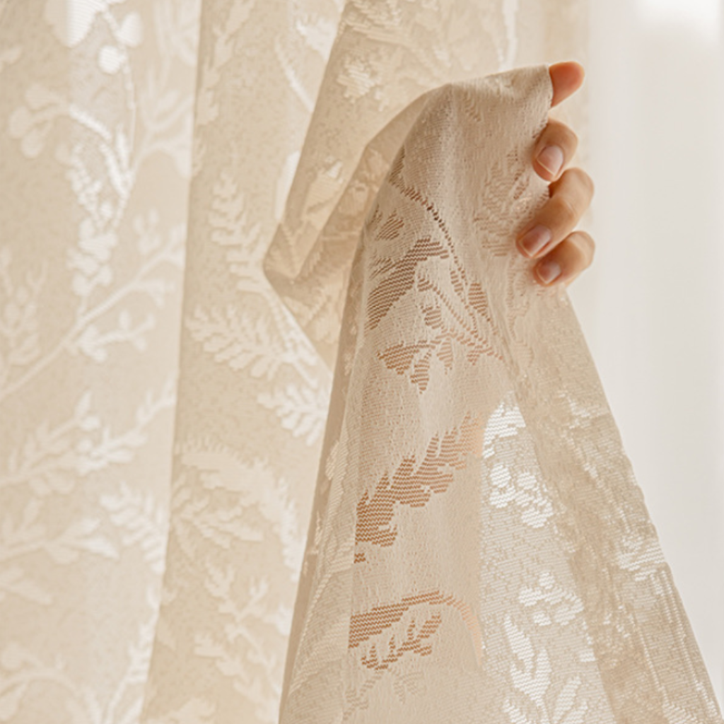 Cream lace drapery panel held by a hand against a light background