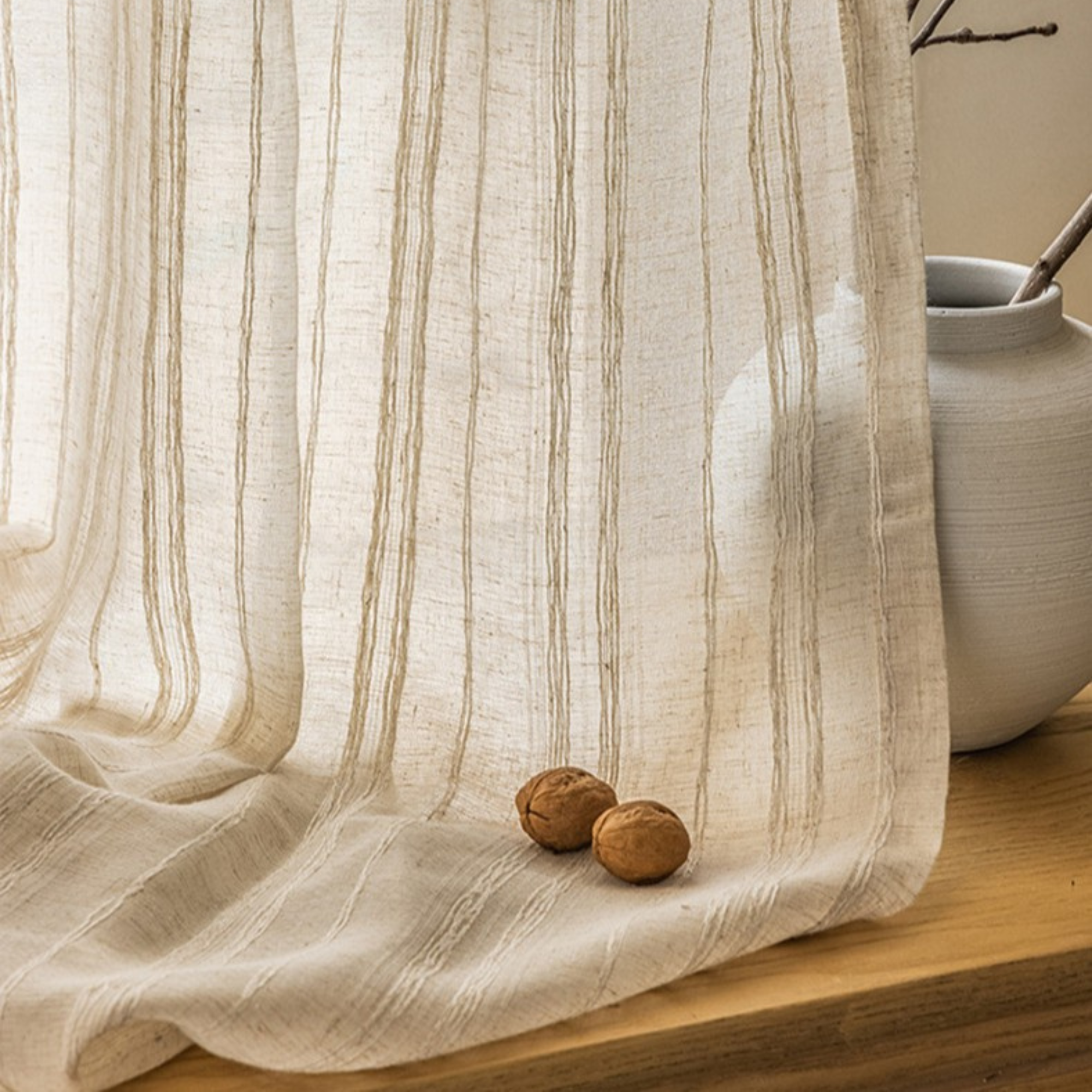 Sheer woven stripe linen curtain with natural patterns on a wooden surface with a ceramic pot and walnuts.