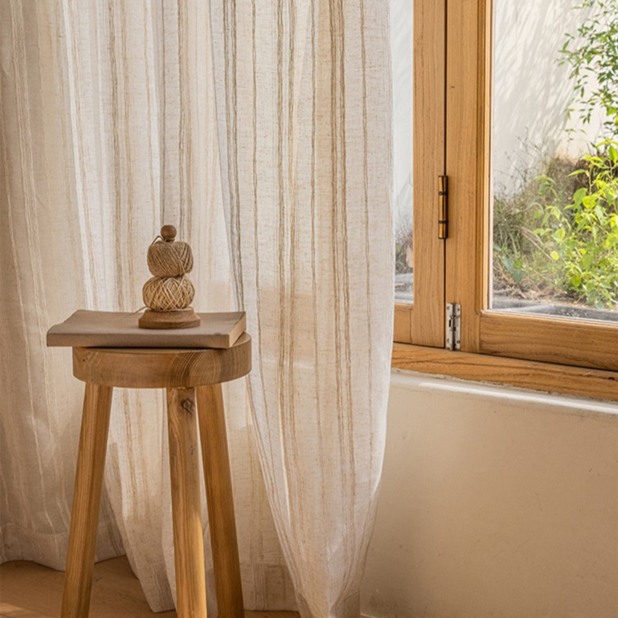 Wooden stool with decorative object in front of a window with wove stripe linen sheer curtains