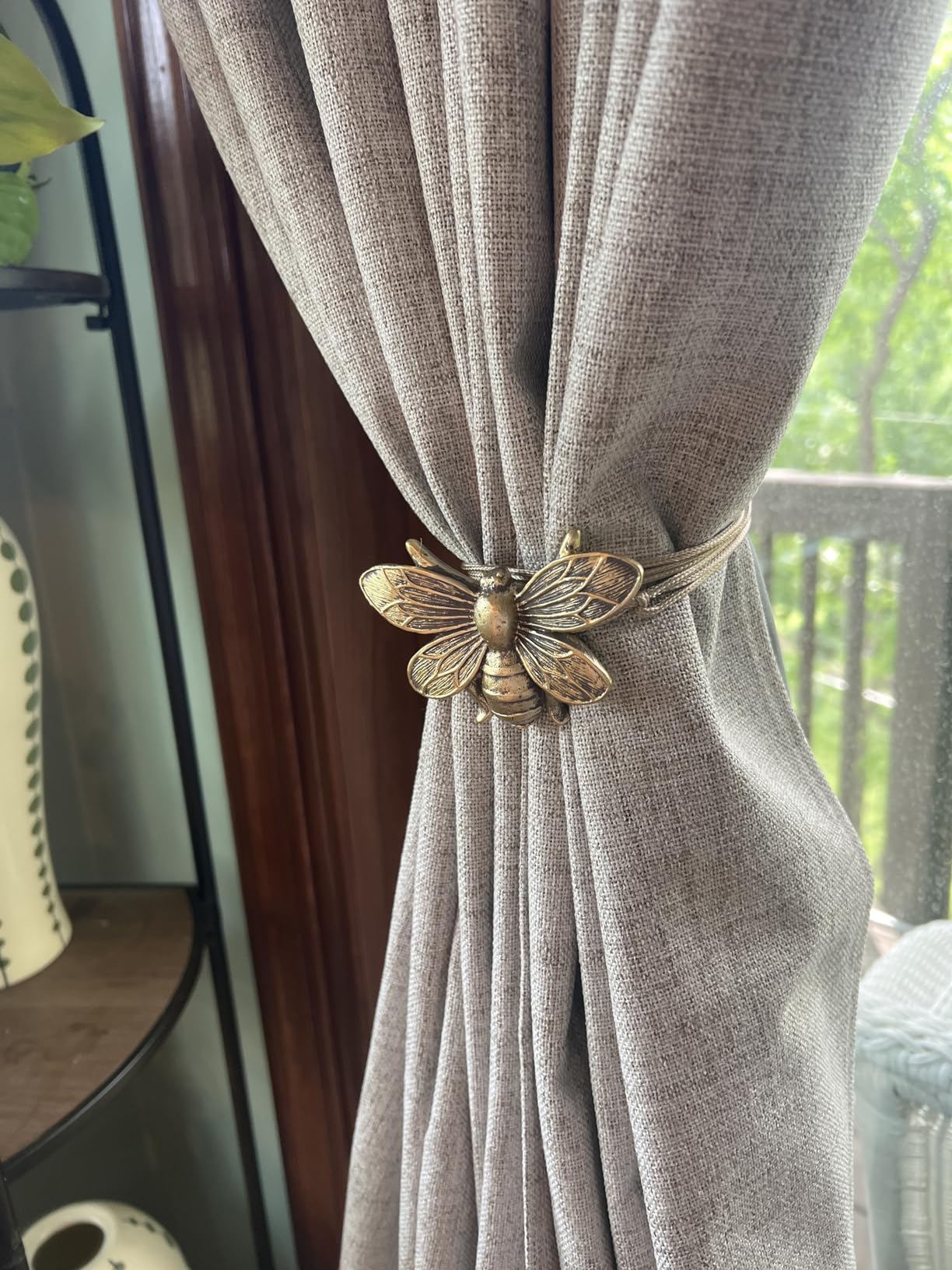 Brown curtain with a decorative gold bumblebee curtain tieback against a blurred indoor background