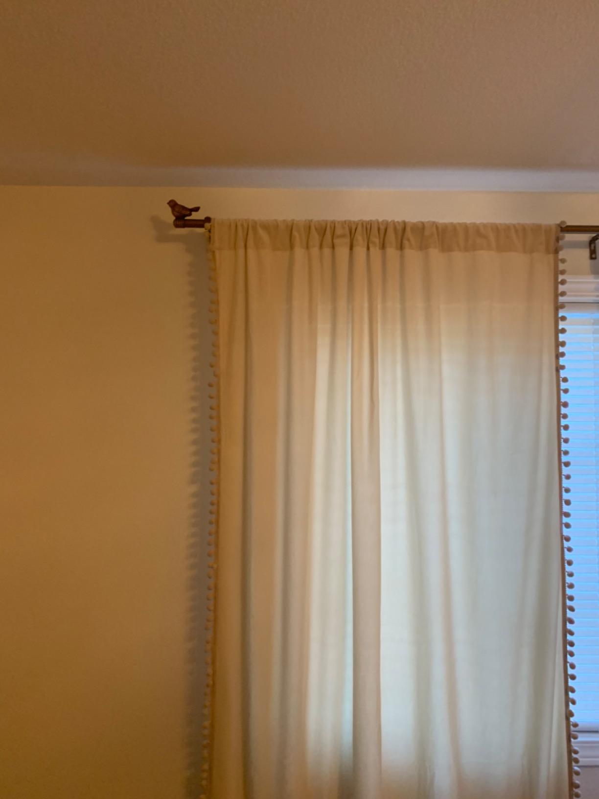 Beige curtain hanging on a decorative bird end rod against a beige wall