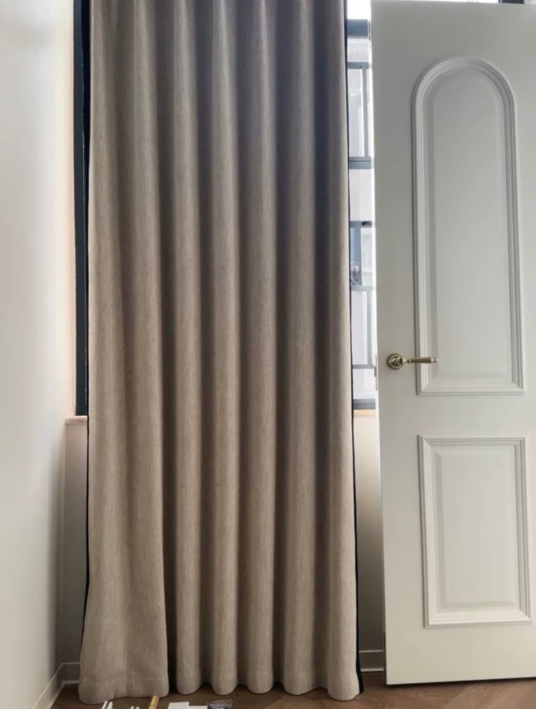 Beige curtain partially drawn in a room with a white door.