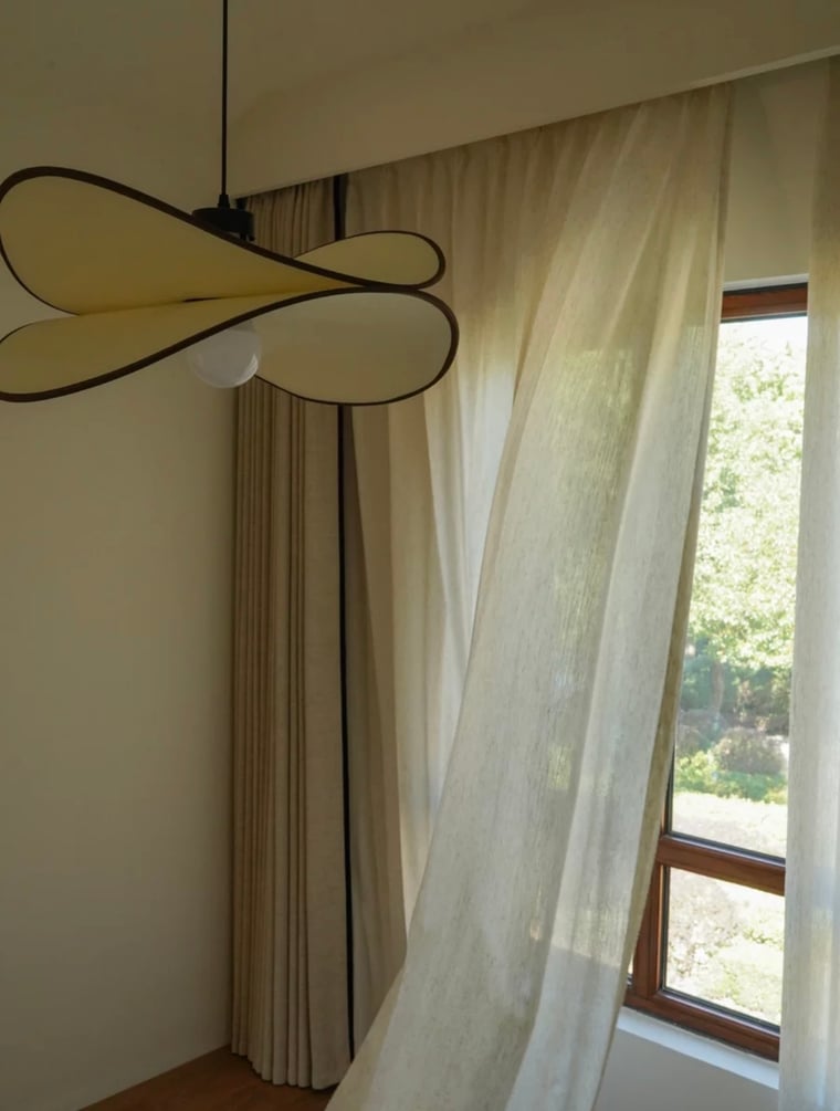 Modern ceiling light fixture in a room with custom cream curtains with black trim and a window.