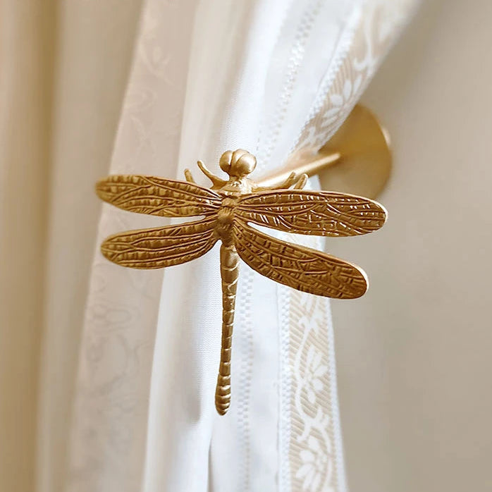 Gold dragonfly-shaped curtain holdback on a white curtain with