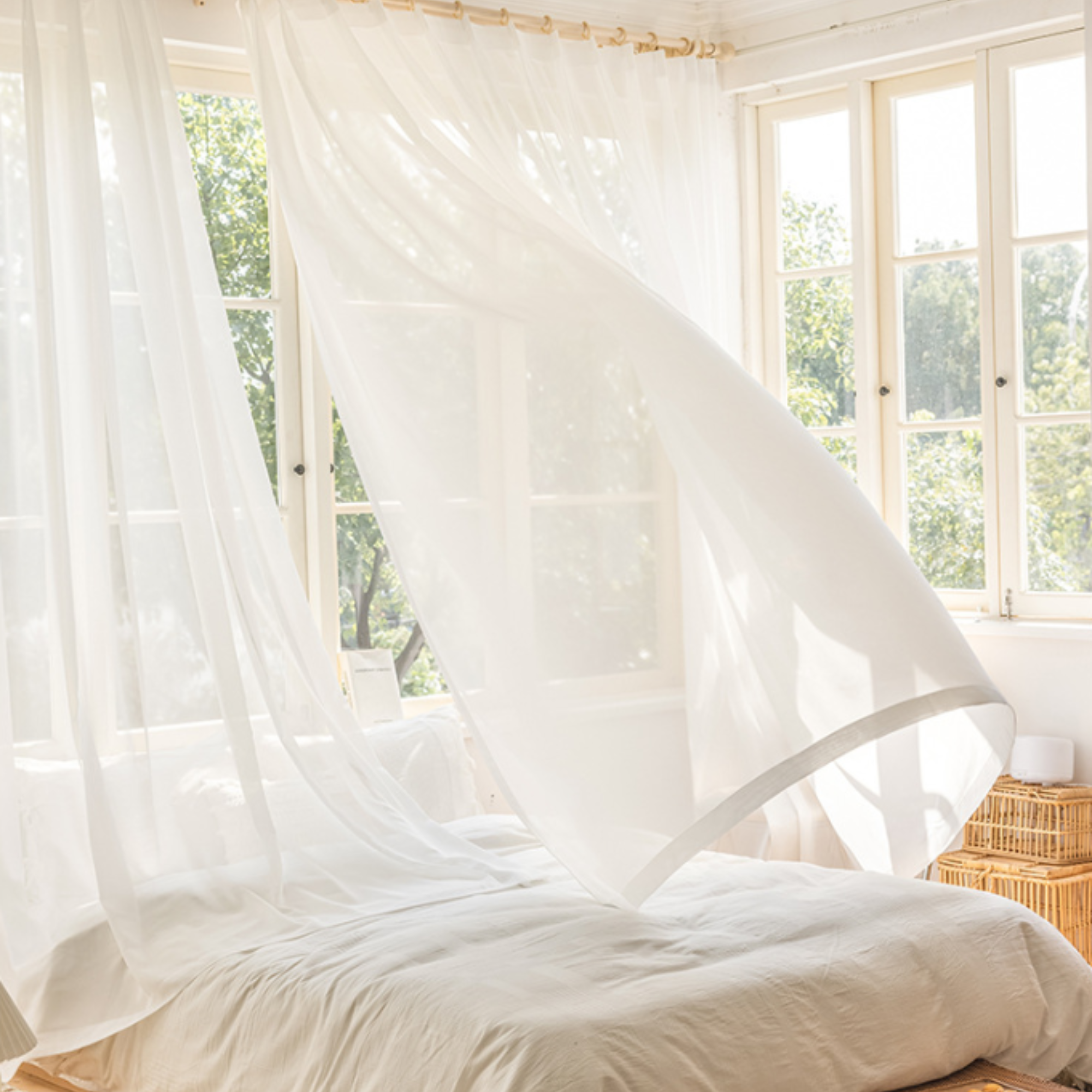 Large bed with sheer curtains blown by wind in a bright room with large windows.