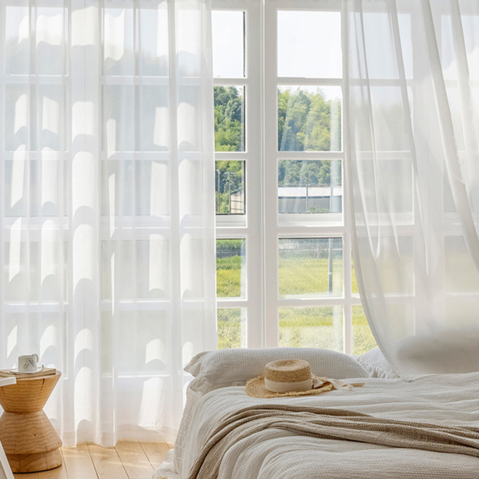 Bedroom with sheer white curtains and a view of greenery outside.