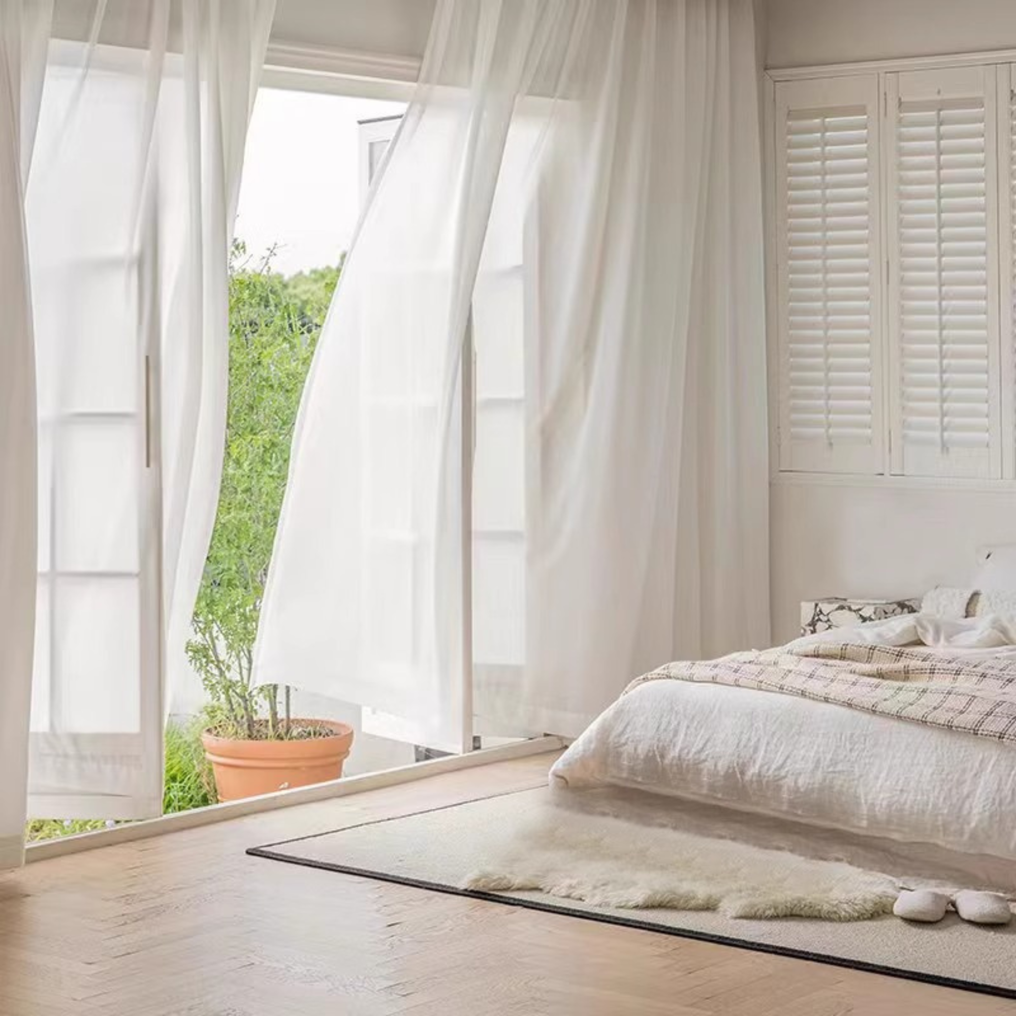Modern bedroom with white bedding, light wood flooring, and sliding glass door with sheer curtains.