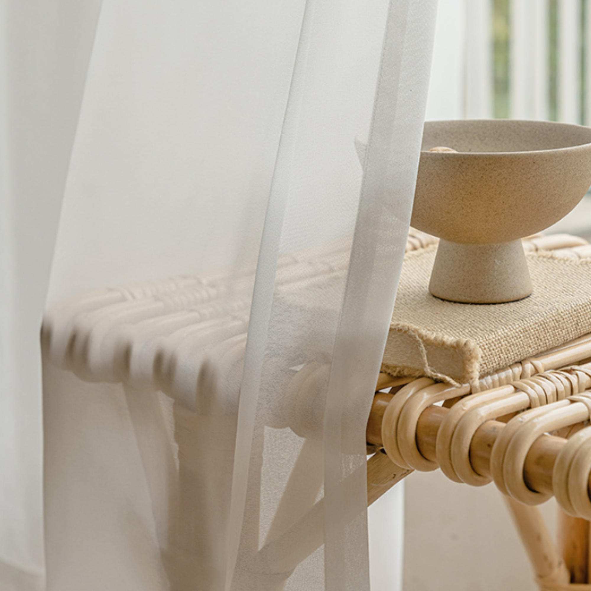 Beige bowl on a woven chair with sheer white curtains in the background