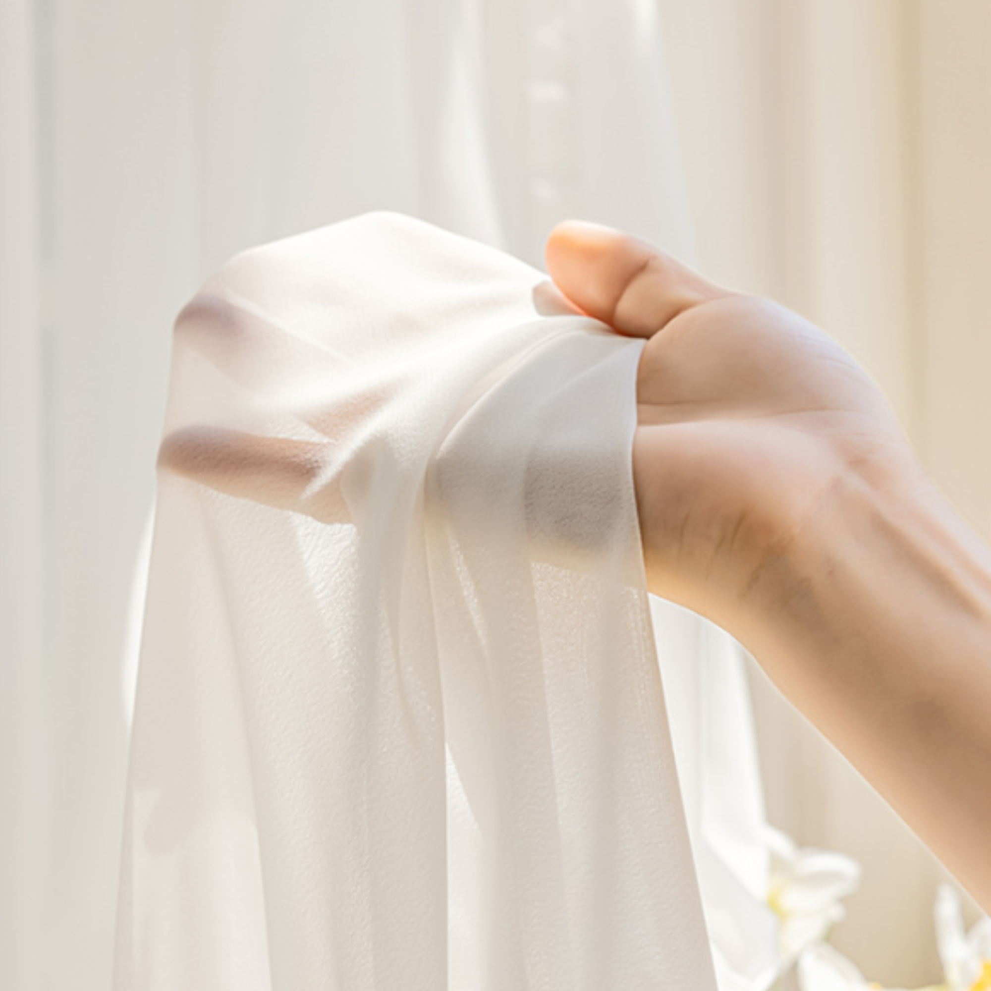 Hand holding a white sheer fabric against a light background, showing its see through quality.
