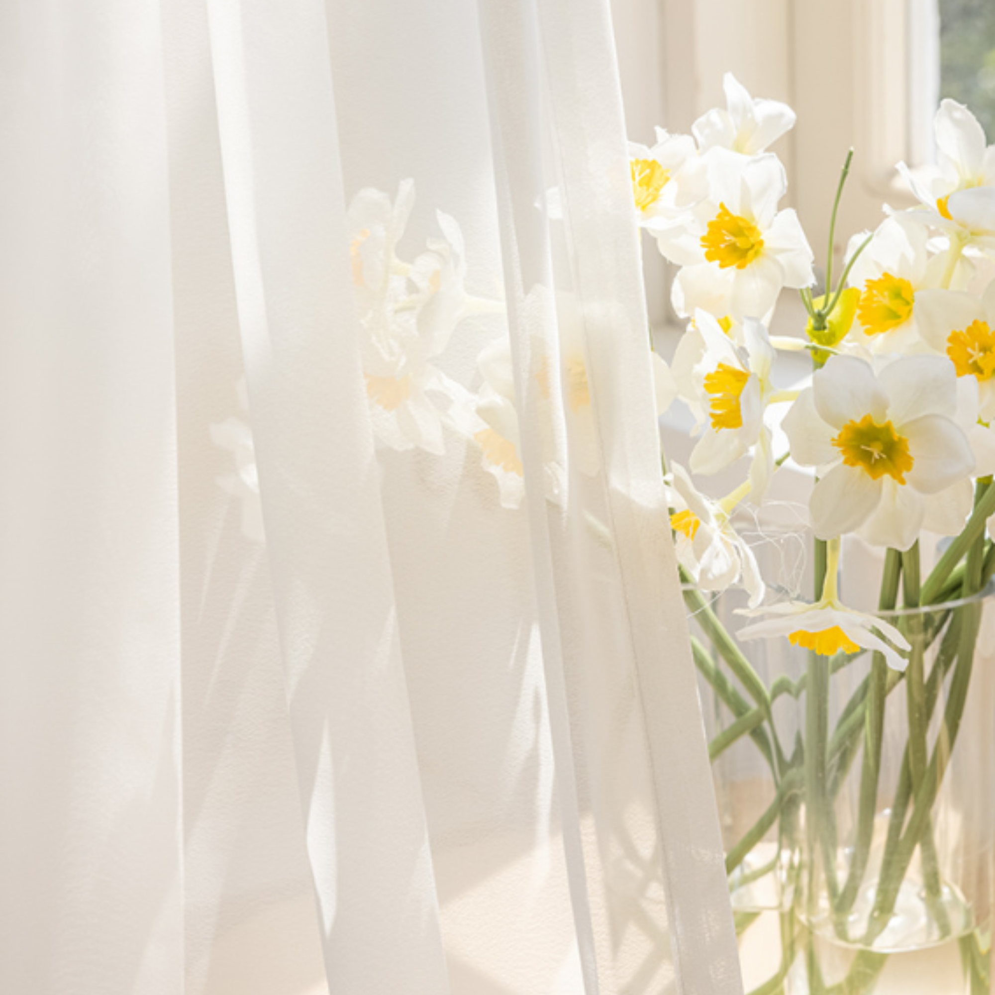 You are able to see yellow and white flowers behind the white sheer curtains.