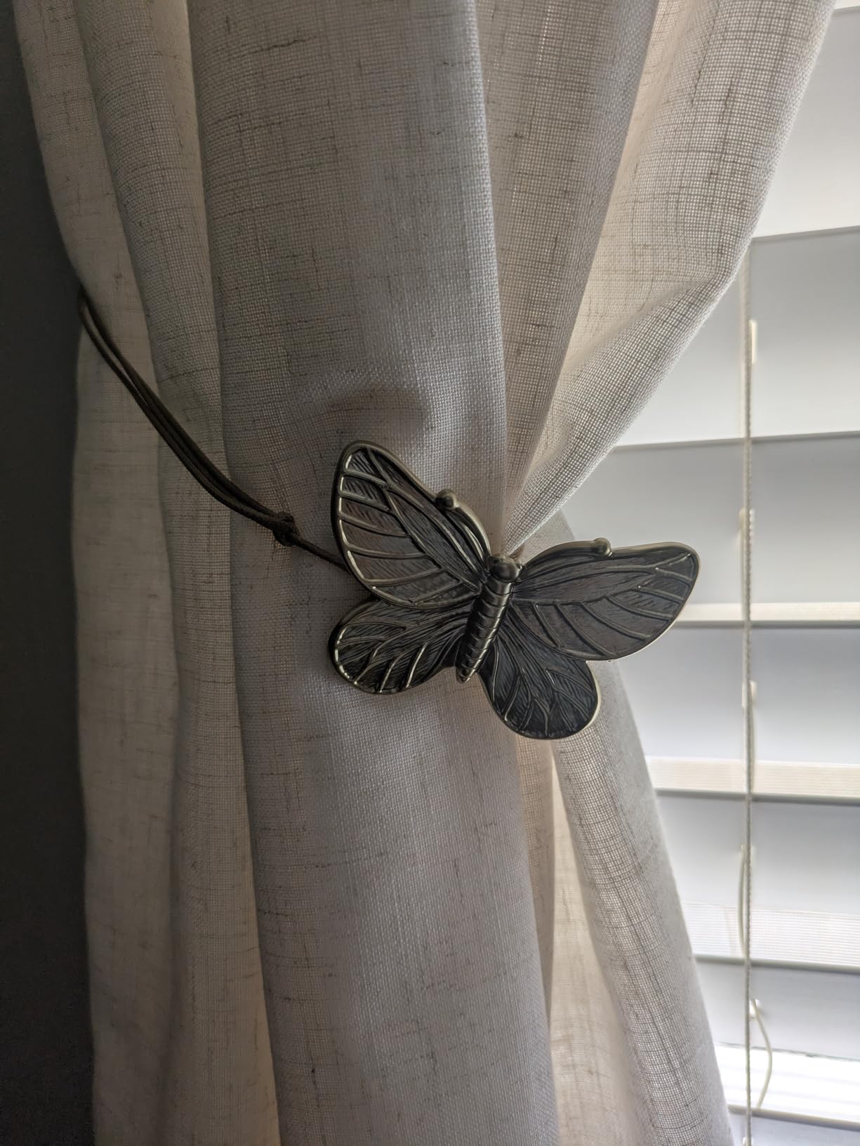 Butterfly-shaped curtain tieback on a beige curtain with a window in the background