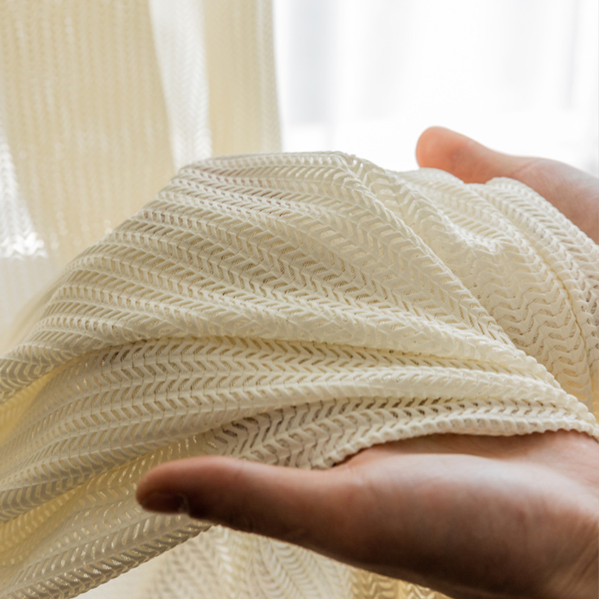 Hand holding a cream colored cat proof fabric with a blurred background