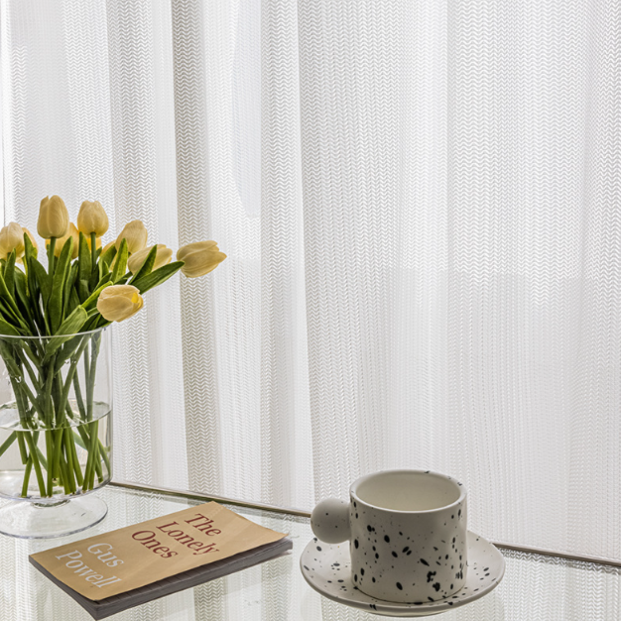 White tulips in a vase on a glass table with a white cat proof sheer curtain in the background