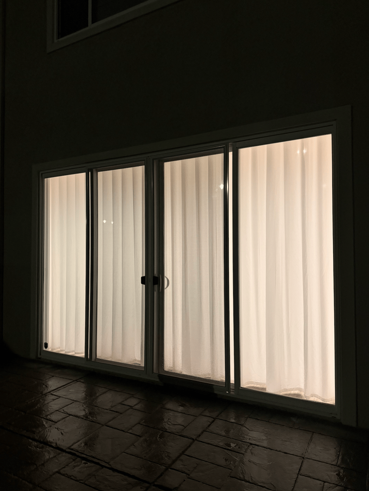 Photo shot from outside of the sliding glass door, showing white privacy curtains that provides complete privacy at night.