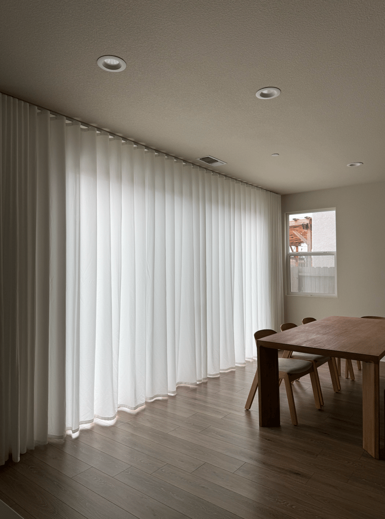 Modern interior with white privacy protecting custom curtains, wooden table, and chairs.