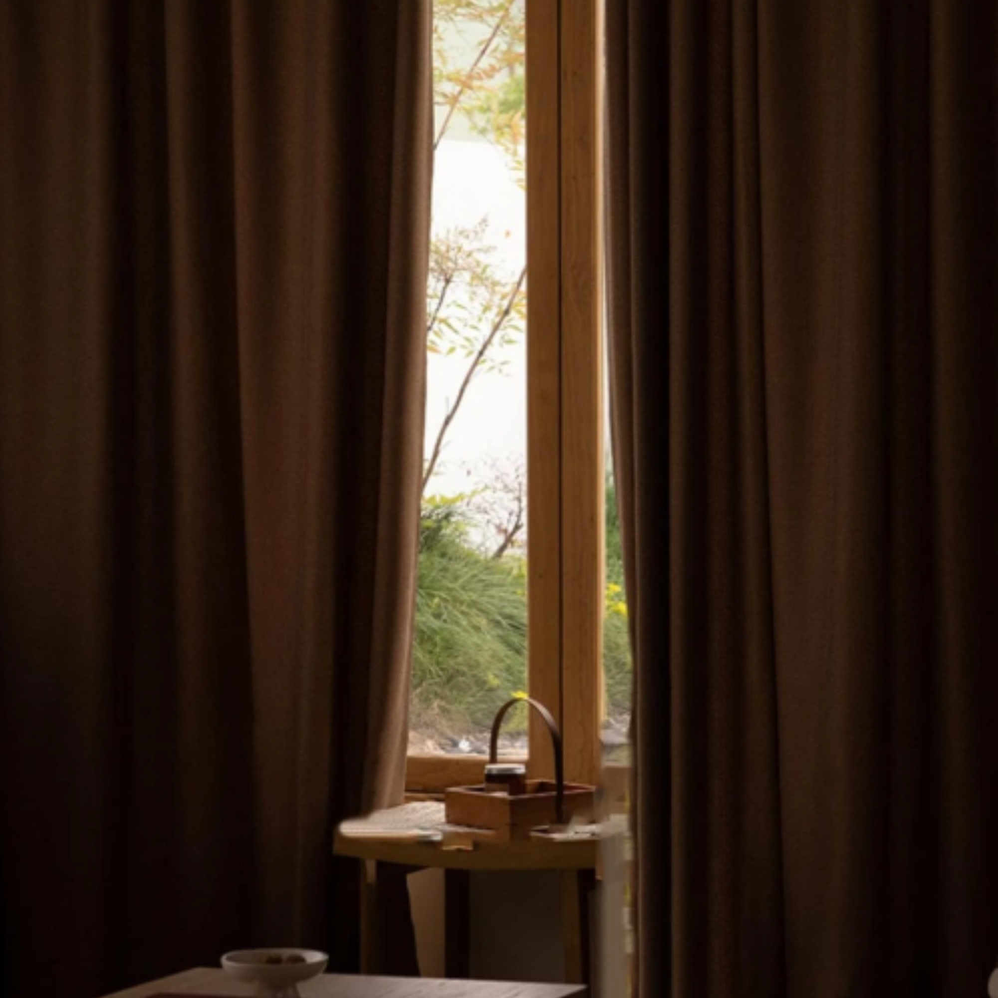 Window with brown herringbone curtains and a view of greenery outside, showing the light blocking ability of the curtains.