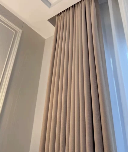 Beige herringbone room darkening curtain hanging in a room with a light gray wall.