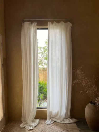 A pair of linen sheer curtains draping on the floor with a rod pocket header style, creating effortless elegance.