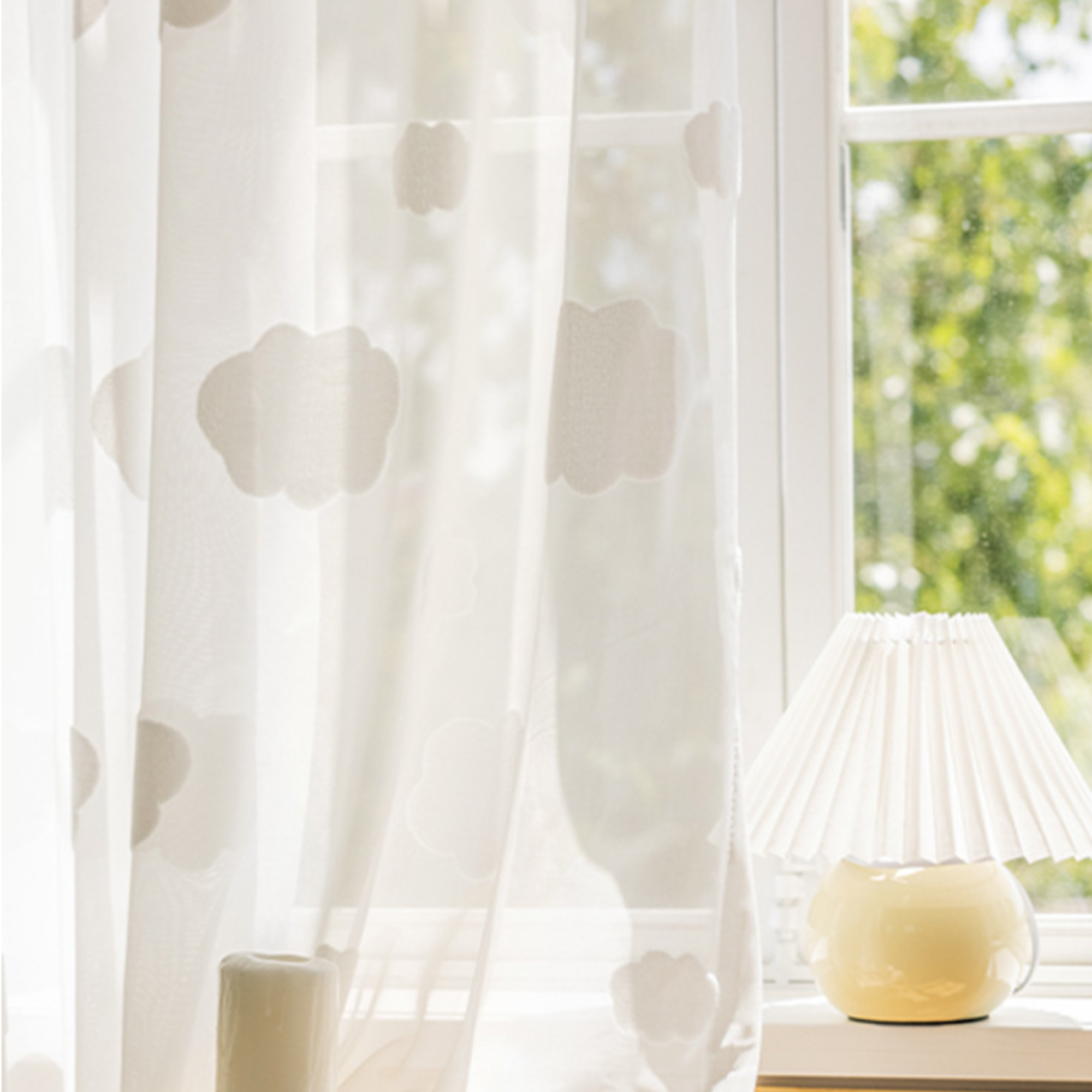 Sheer white curtains with a 3d cloud pattern in front of a window with a view of greenery.